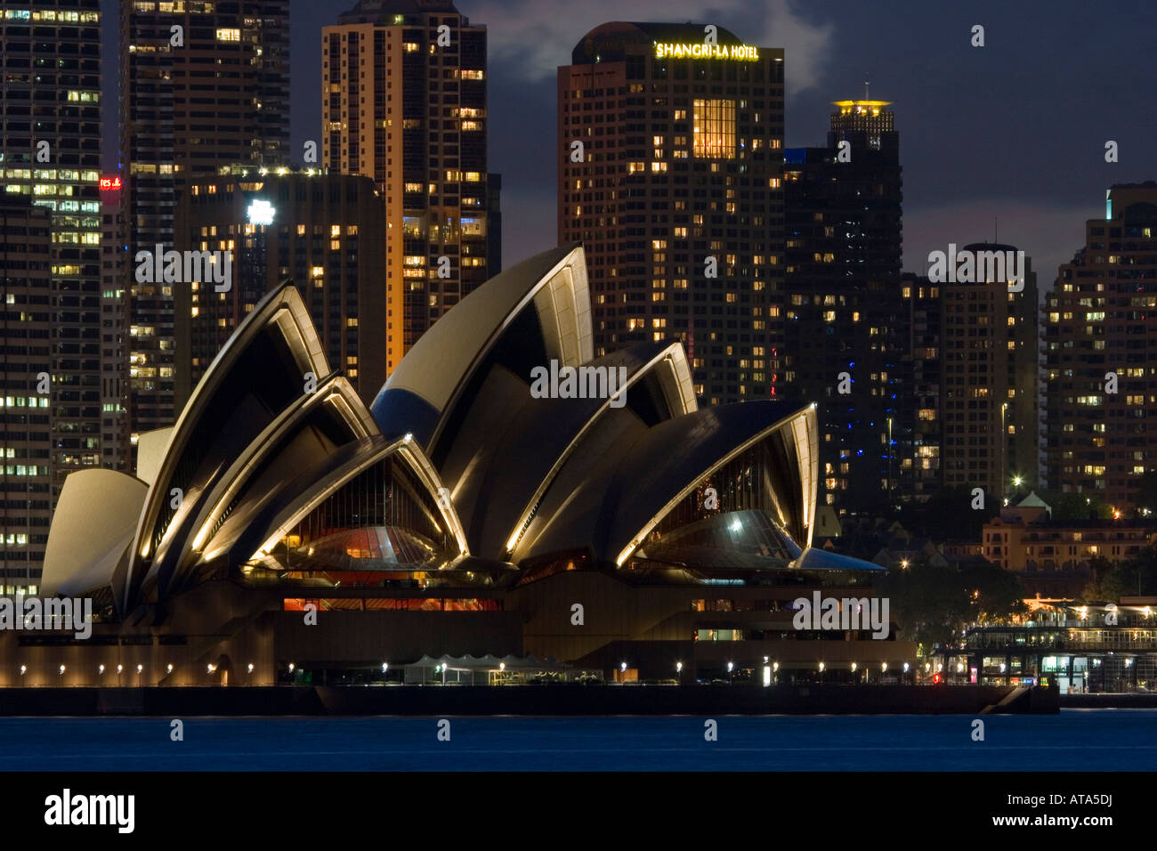 Una notte illuminata scena guardando attraverso il porto di Sydney per l'iconica Opera House di Sydney, Australia. Foto Stock