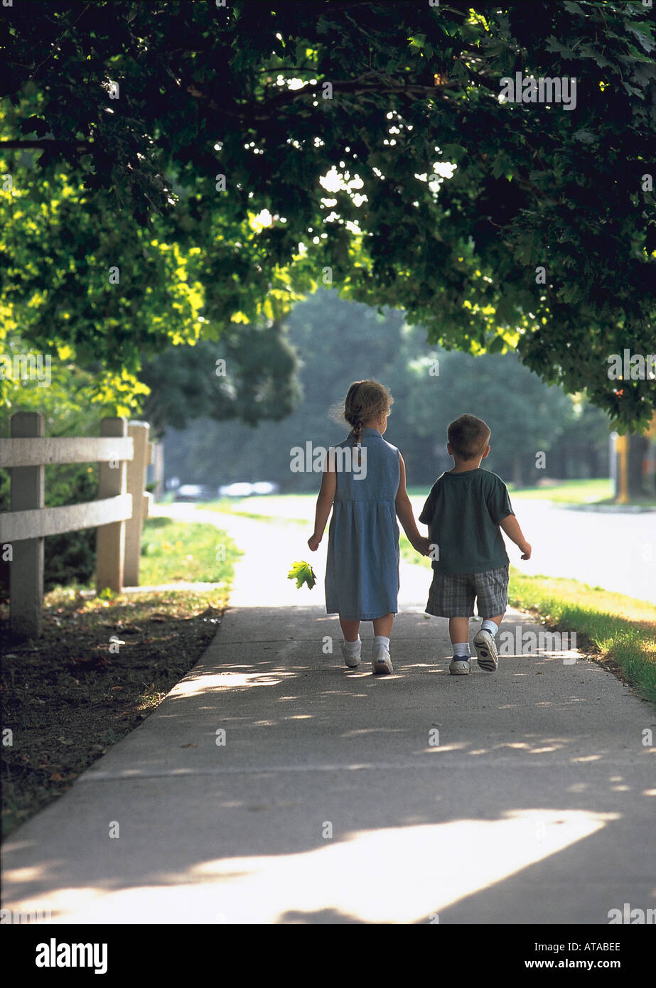 Due bambini piccoli a camminare sul marciapiede tenendo le mani Foto Stock