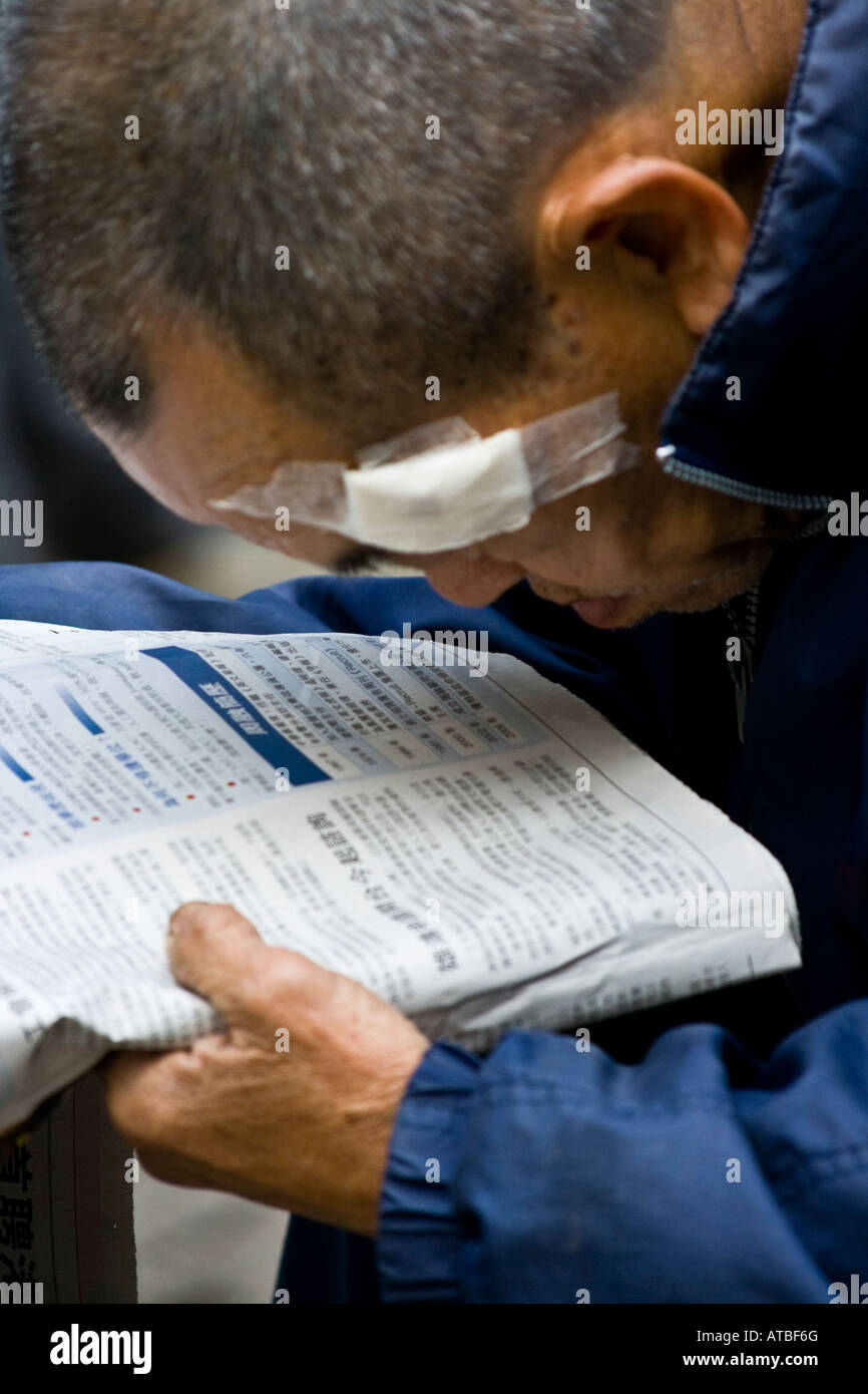 Un lungimirante vecchio uomo cinese leggendo un giornale in centro a Hong Kong Foto Stock
