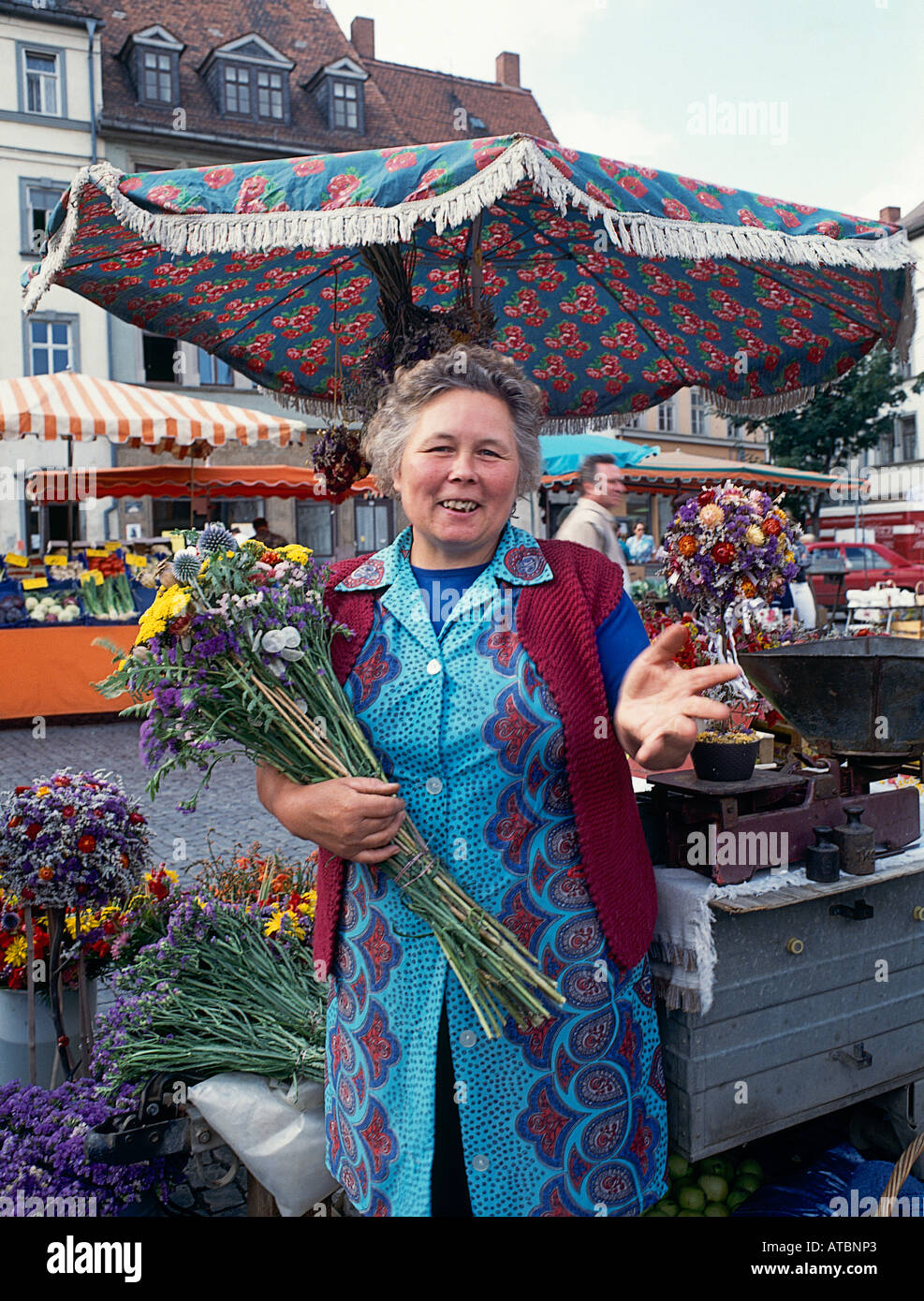 Un sorridente commerciante femmina che offre un grande mazzo di fiori per la vendita dalla sua stalla nel mercato della città di Weimar in Germania orientale Foto Stock