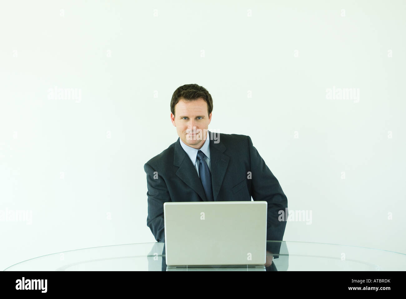 Imprenditore seduto alla scrivania, utilizzando il computer portatile, sorridente in telecamera Foto Stock