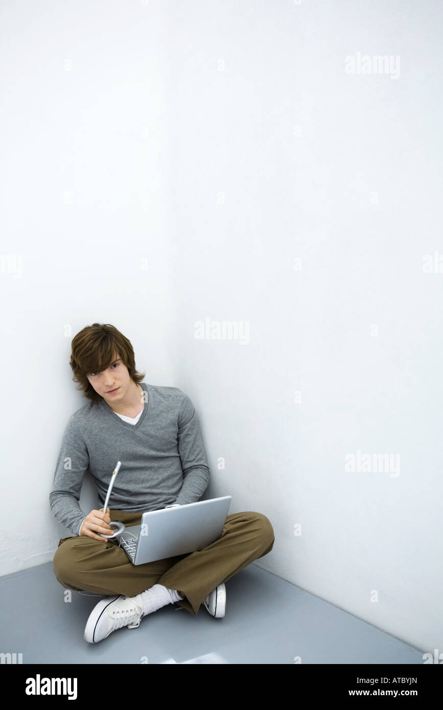 Giovane uomo seduto a terra, utilizzando il computer portatile e il microfono, guardando la fotocamera Foto Stock