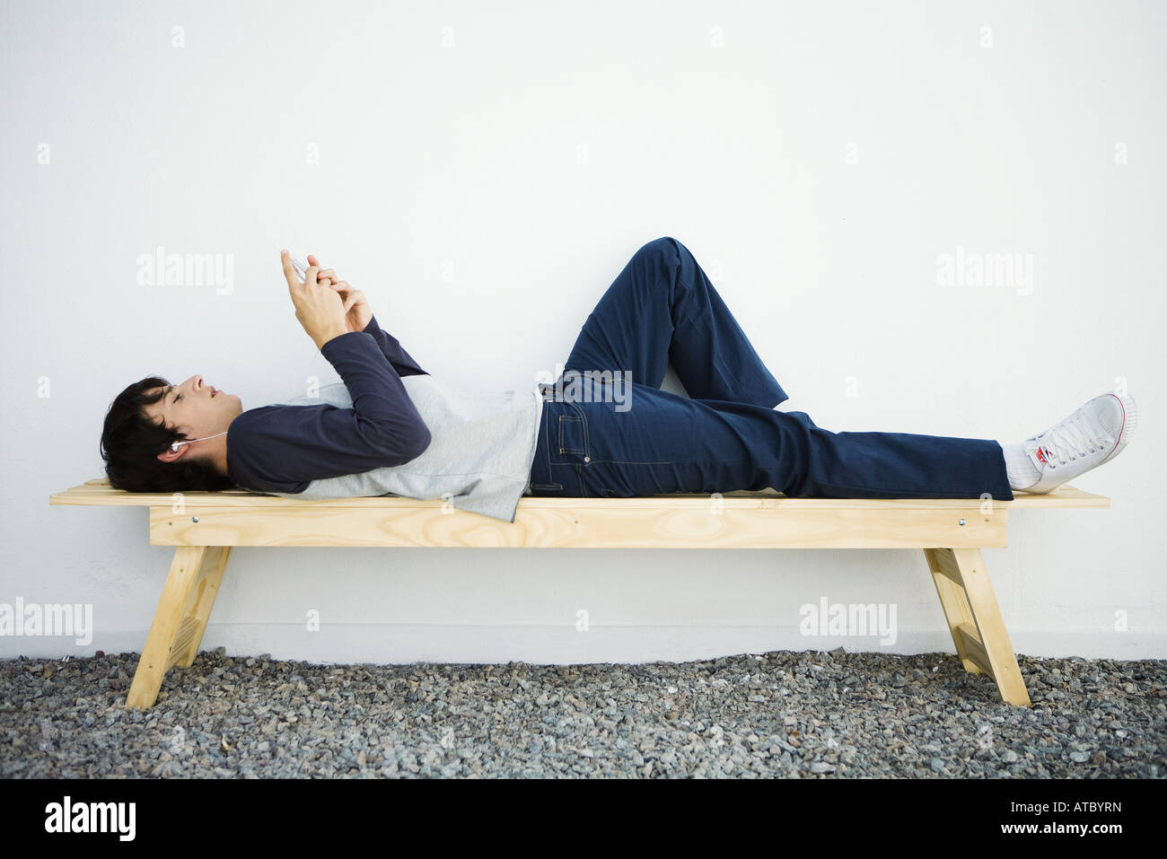 Giovane uomo disteso su un banco di lavoro, con l'ascolto di MP3 player,  vista laterale Foto stock - Alamy
