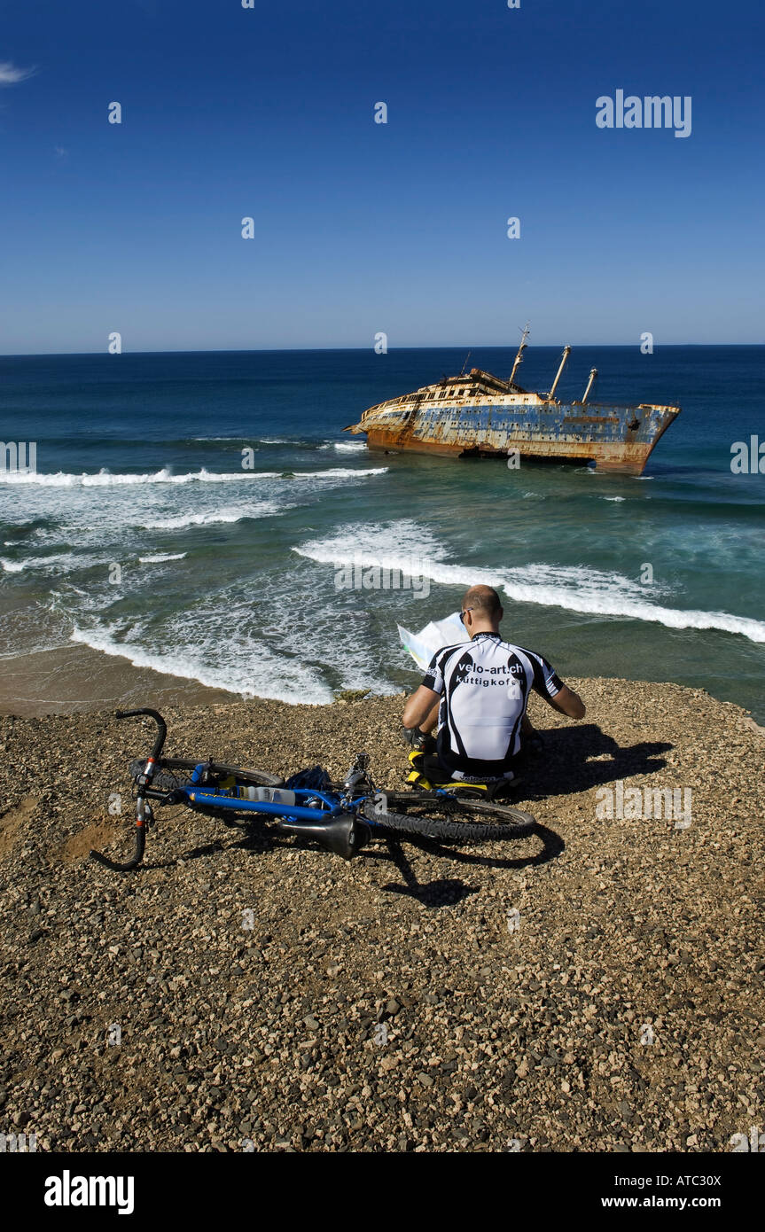 Ciclista seduti in barca relitto della American star in Fuerteventura Spagna la lettura di una mappa dal mare. Foto Stock