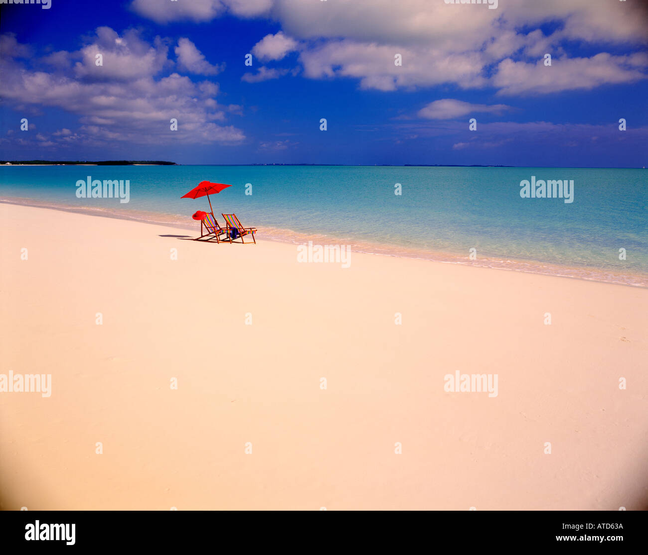 Scena tropicale di due colorate sedie a sdraio e un ombrellone seduti al bordo delle acque in Bahamas Foto Stock