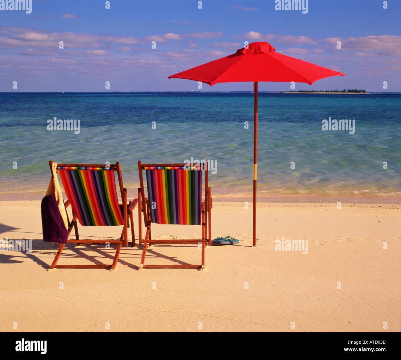 Scena tropicale di due colorate sedie a sdraio e un ombrellone seduti ad acqua s edge in Bahamas Foto Stock