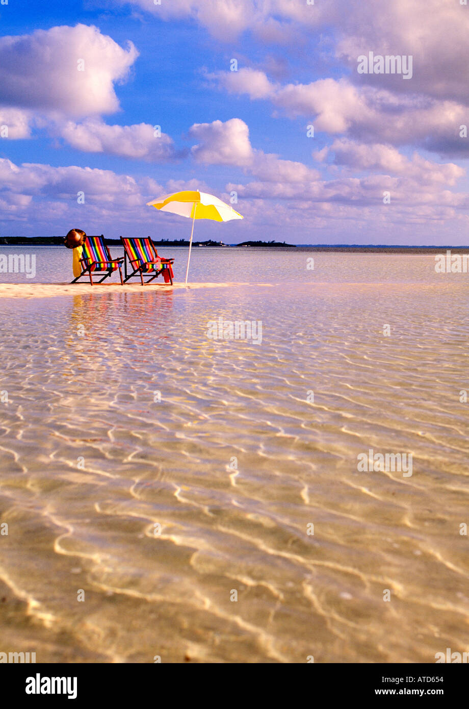 Sedie a sdraio e un ombrellone giallo a sedersi su una spiaggia rivolta verso le acque cristalline del Mar dei Caraibi alle Bahamas Foto Stock