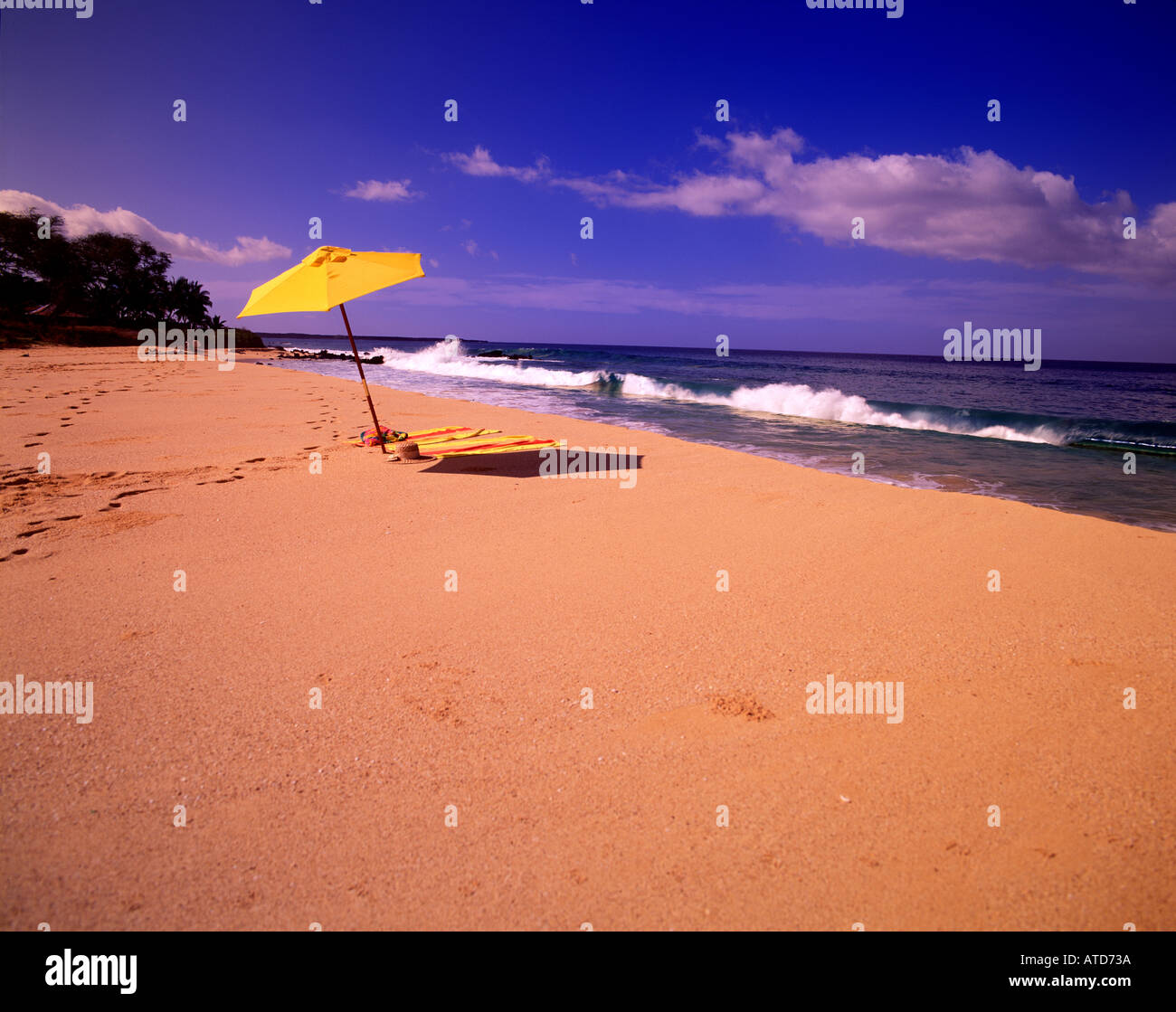 Un ombrello giallo si siede nella sabbia della spiaggia di Makina Maui Hawaii come le onde in rotolo Foto Stock