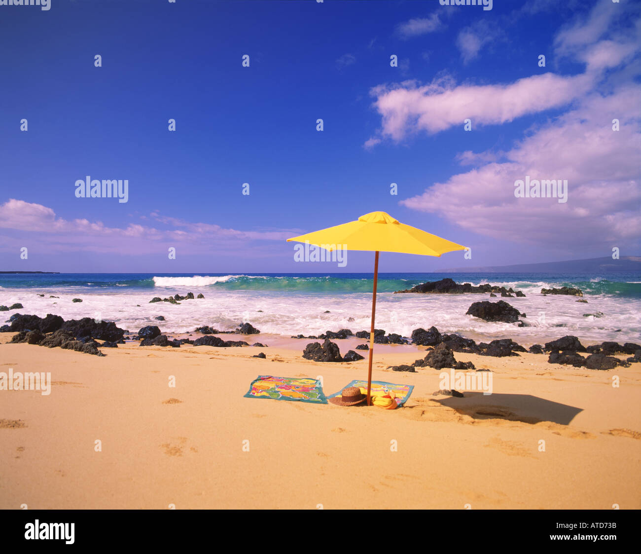 Un ombrello giallo si siede nella sabbia della spiaggia di Makina Maui Hawaii come le onde che si infrangono sulla spiaggia rocciosa Foto Stock