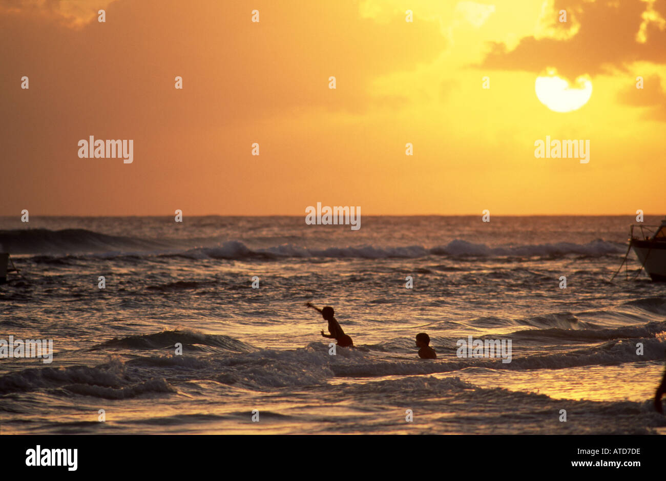 Due persone wade attraverso le onde come il sole che tramonta in Barbados Foto Stock