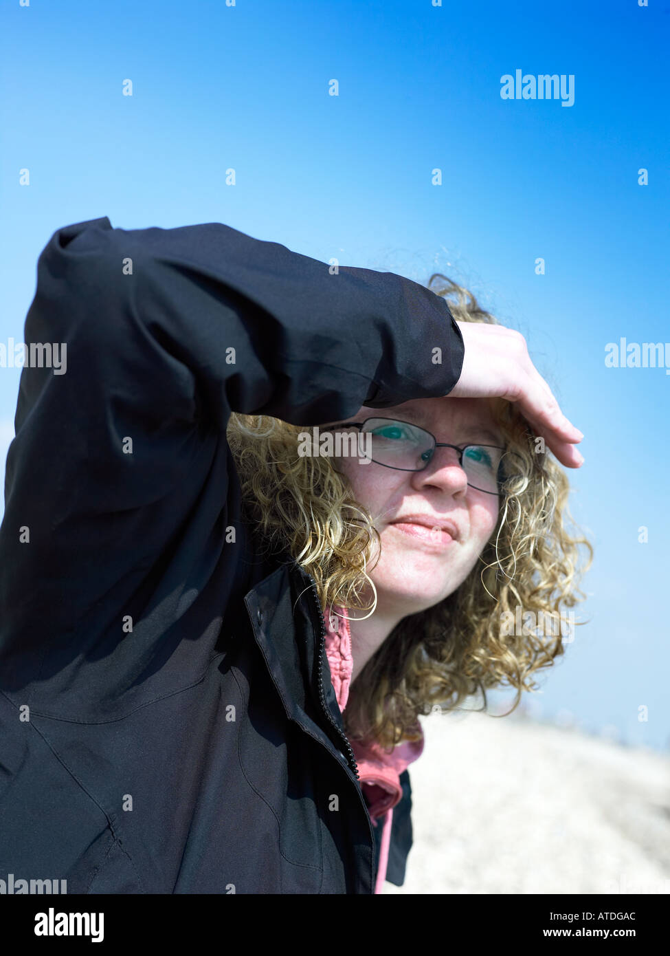 Giovane donna vestita di nero outdoor usura sulla luminosa e soleggiata giornata a cercare qualcosa con la mano alzata fino a protezione occhi da Foto Stock