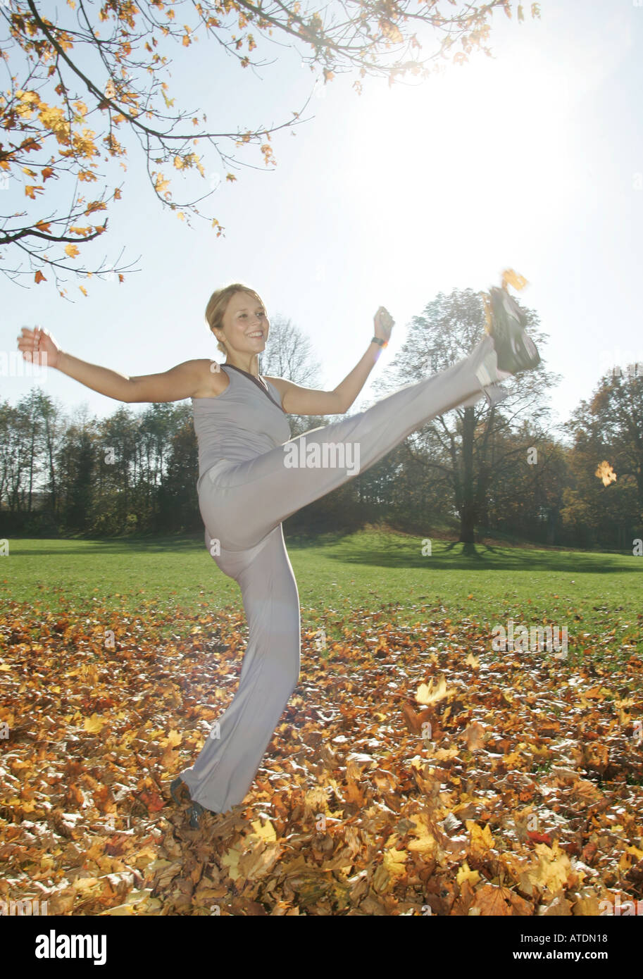 Giovane donna gode di calci in un mucchio di foglie di autunno nel parco Foto Stock