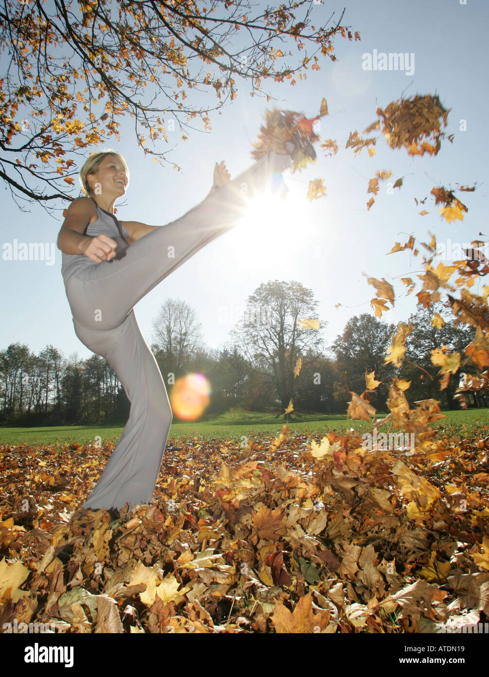 Giovane donna gode di calci in un mucchio di foglie di autunno nel parco Foto Stock