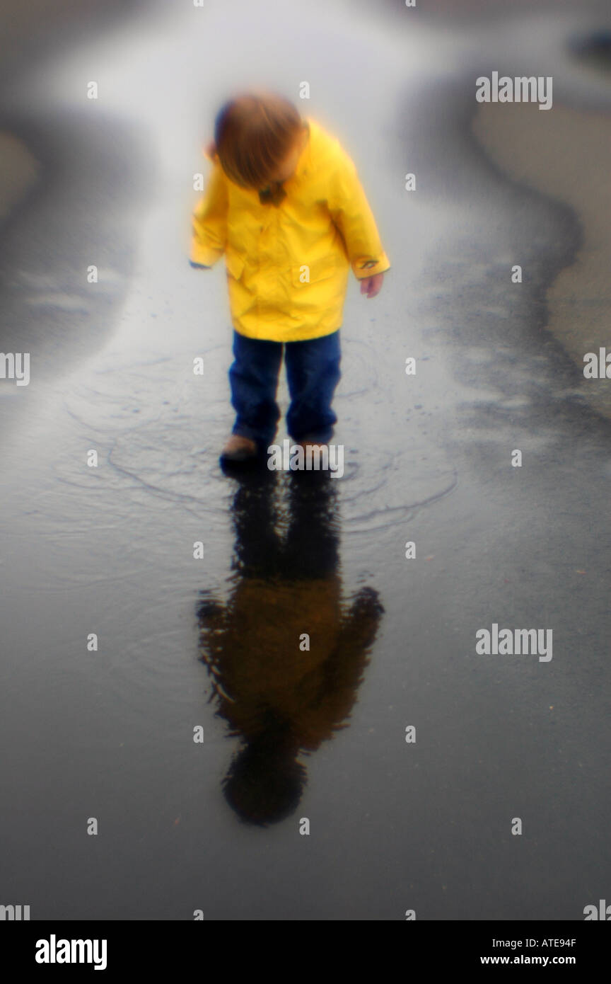 Piccolo ragazzo giocando in una pozza d'acqua pioggia slicker Foto Stock