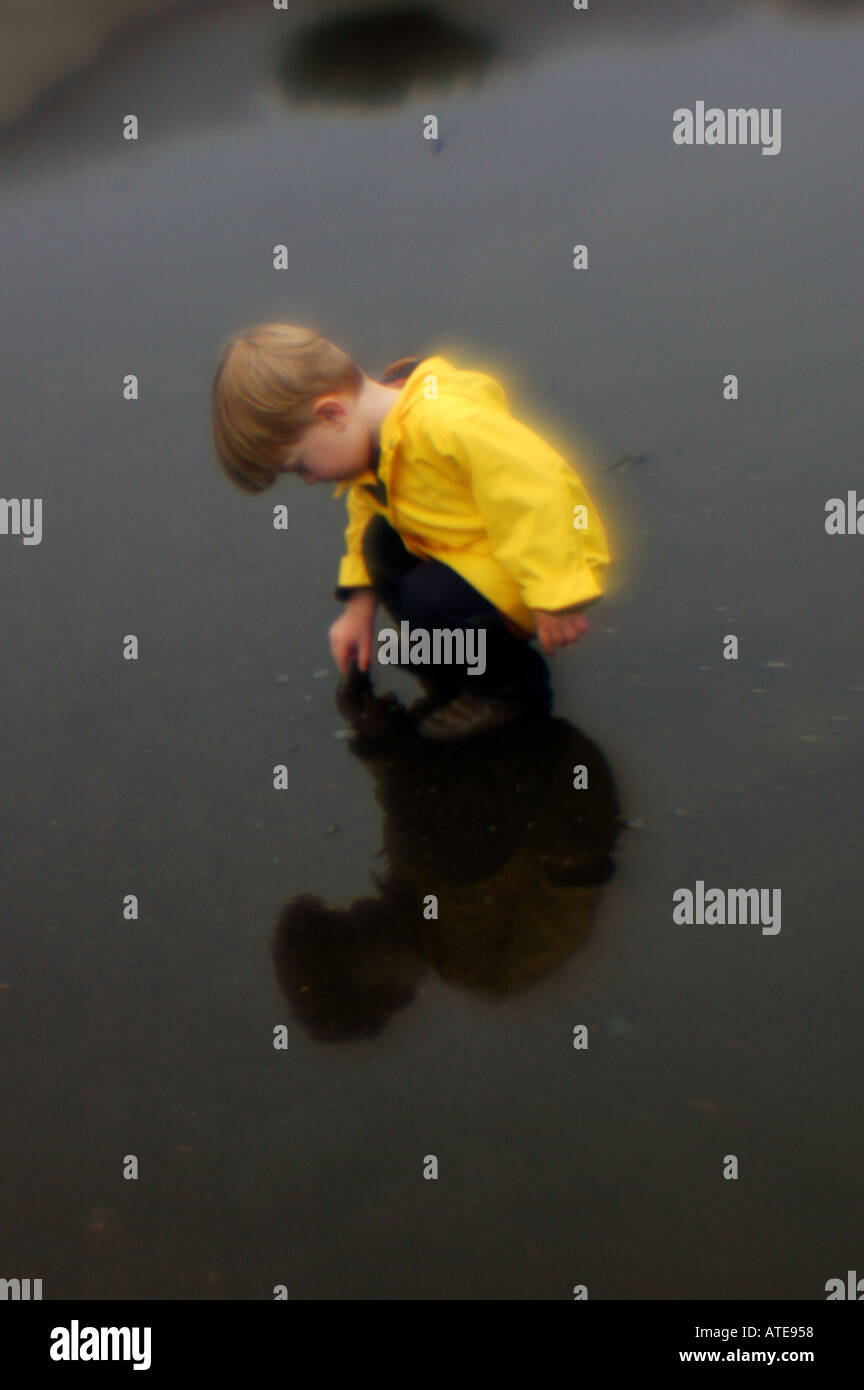 Piccolo ragazzo giocando in una pozza d'acqua indossando giallo Giacca pioggia Foto Stock