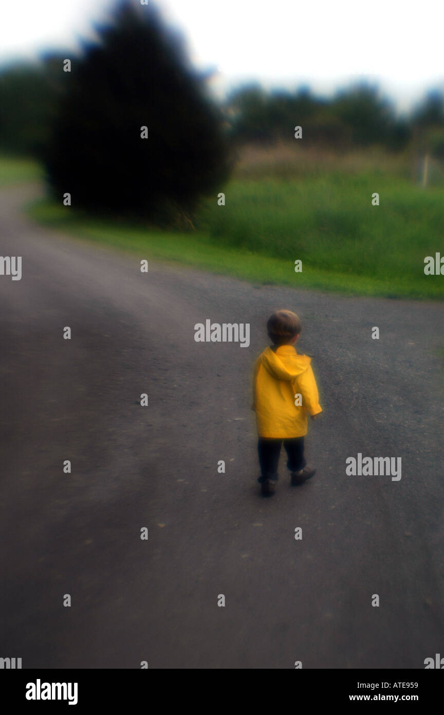 Future Concept piccolo ragazzo camminando verso il basso lungo il piano stradale indossando cappotto giallo Foto Stock