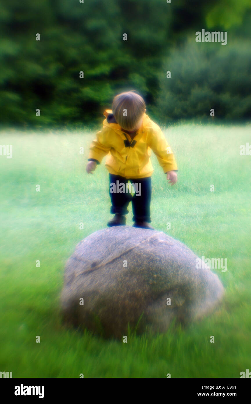 Piccolo Ragazzo in piedi su una roccia a giocare indossando cappotto giallo Foto Stock