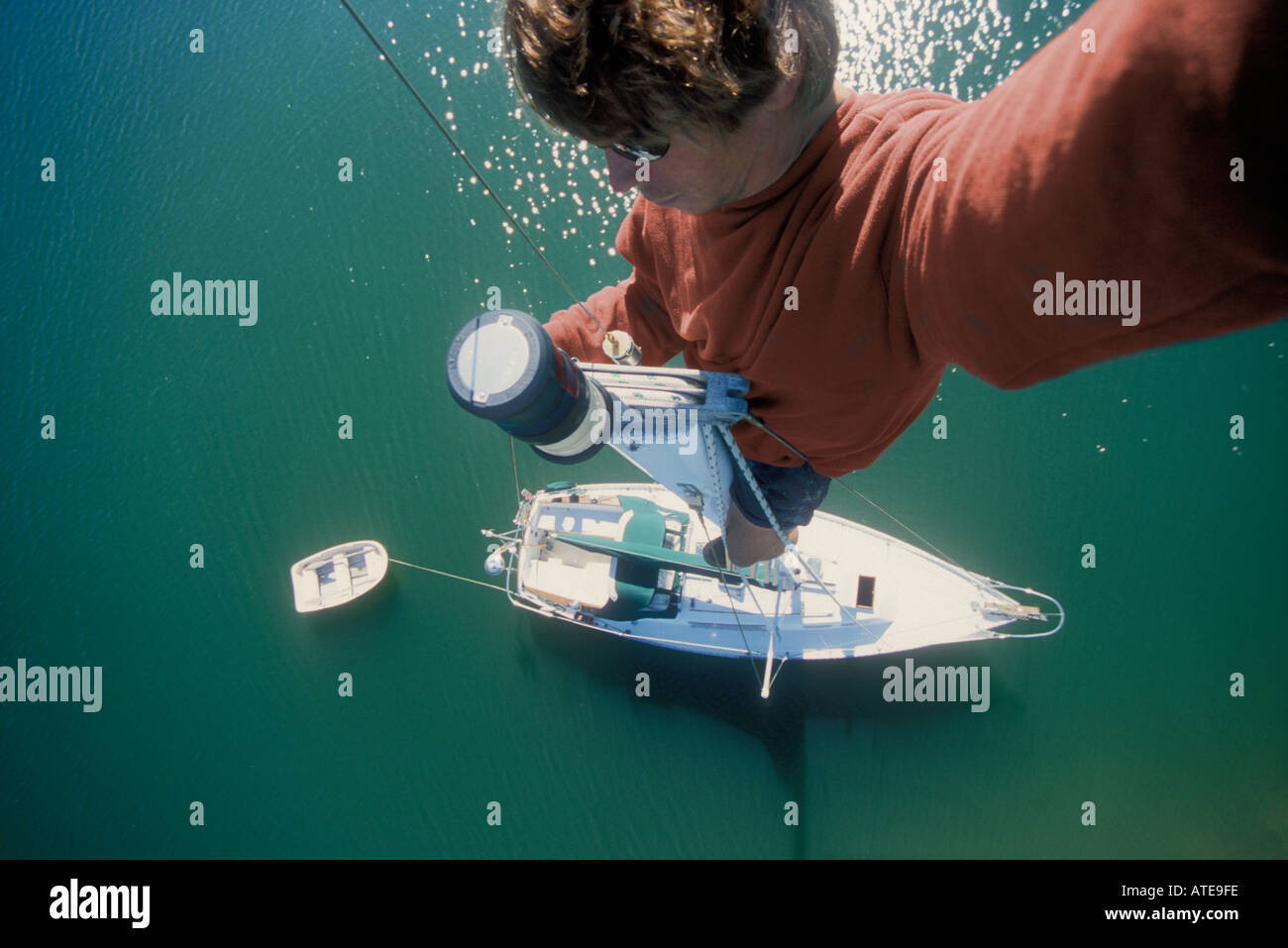 Un uomo nella parte superiore dell'albero di una barca a vela guardando verso il basso sulla testa di palo della luce, deck e gommoni. Foto Stock