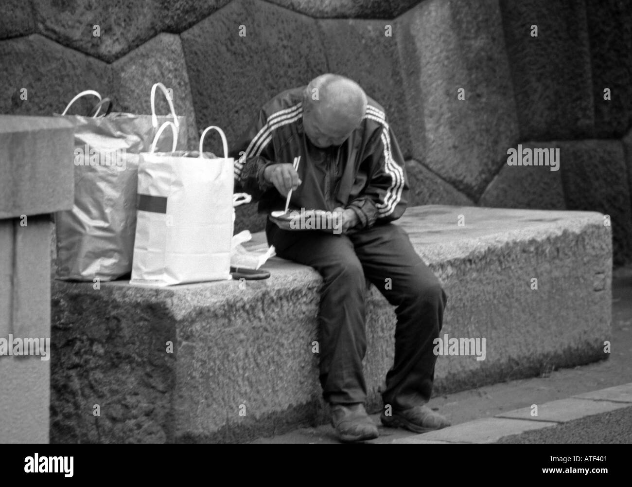 Vecchio senile uomo in grassetto con borse di sedersi sul pubblico banco di calcestruzzo consumano pranzare all'aperto dalla parete di roccia Tokyo Giappone Asia Orientale Foto Stock