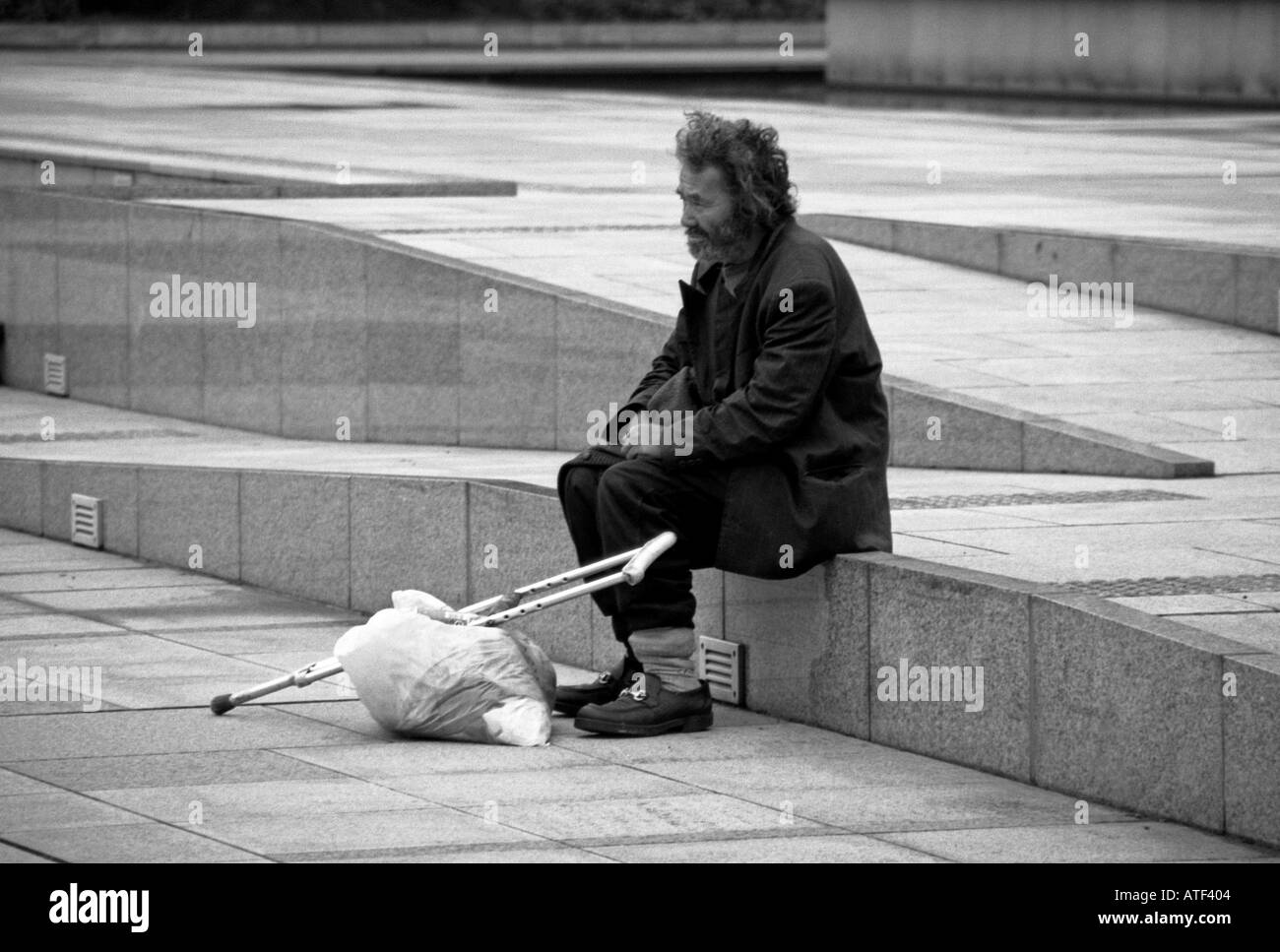 Barbuto uomo senile con borsa & si accovaccia sedersi da solo lonely sulla splendente pavimento in marmo passi di monumento Tokyo Giappone Asia Orientale Foto Stock