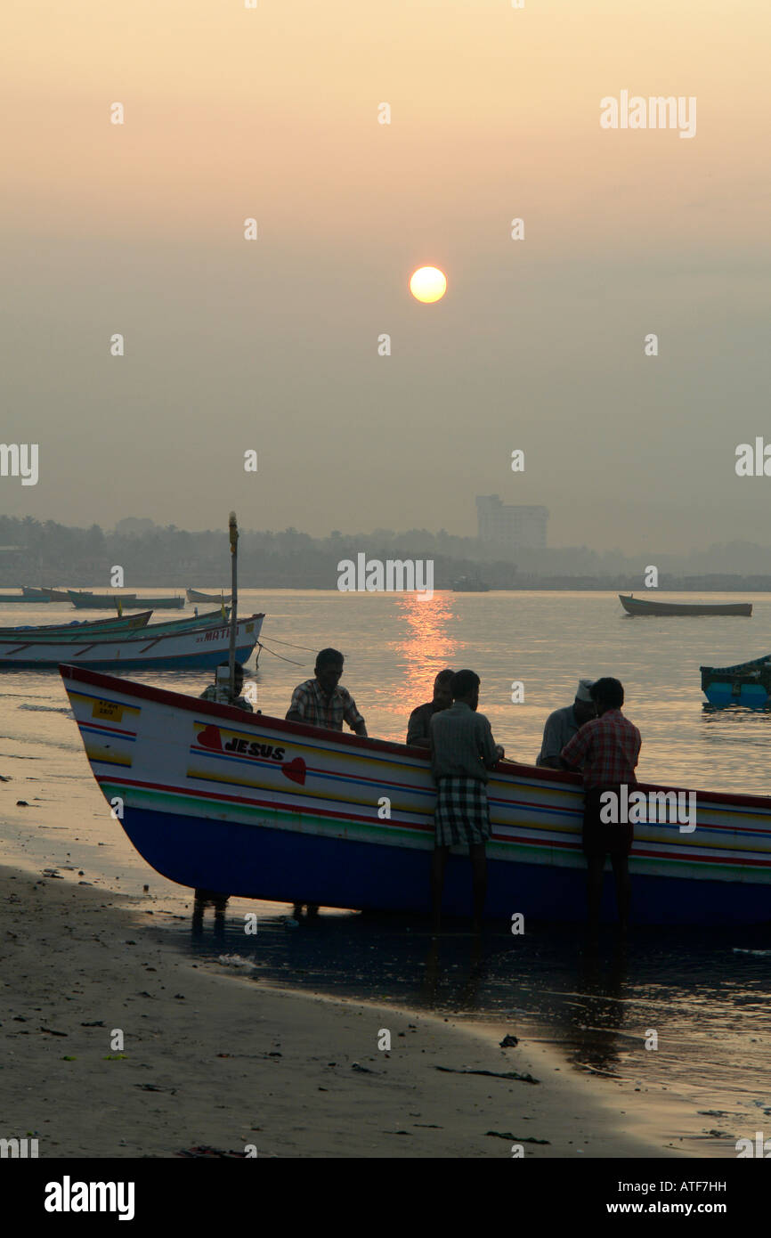 Indiana tradizionale barca da pesca e per i pescatori di controllare le loro reti al sorgere del sole sulla spiaggia di Quilon Foto Stock