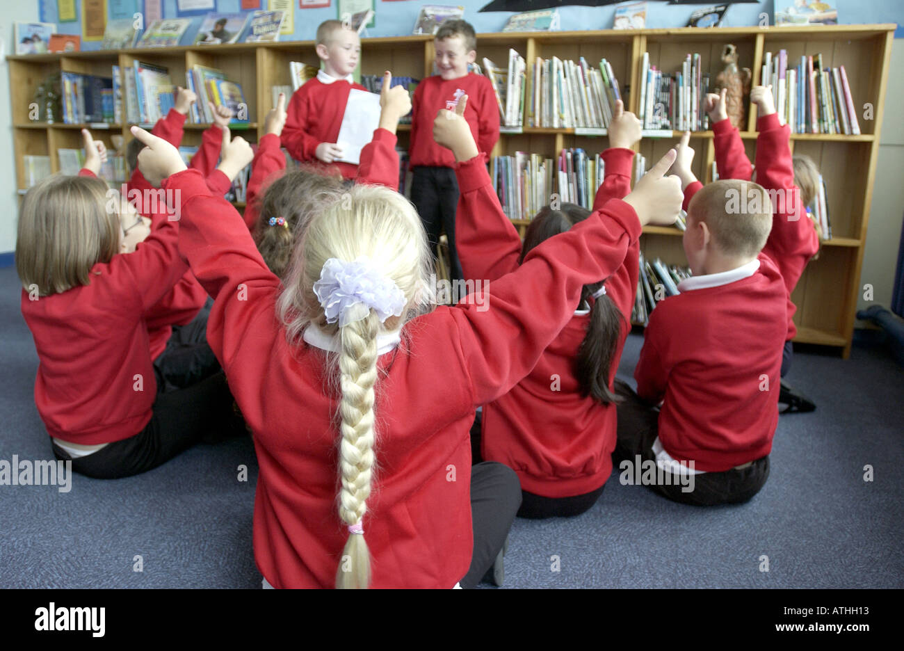 Desiderosi di bambini con le braccia in aria in una scuola primaria classroom Foto Stock