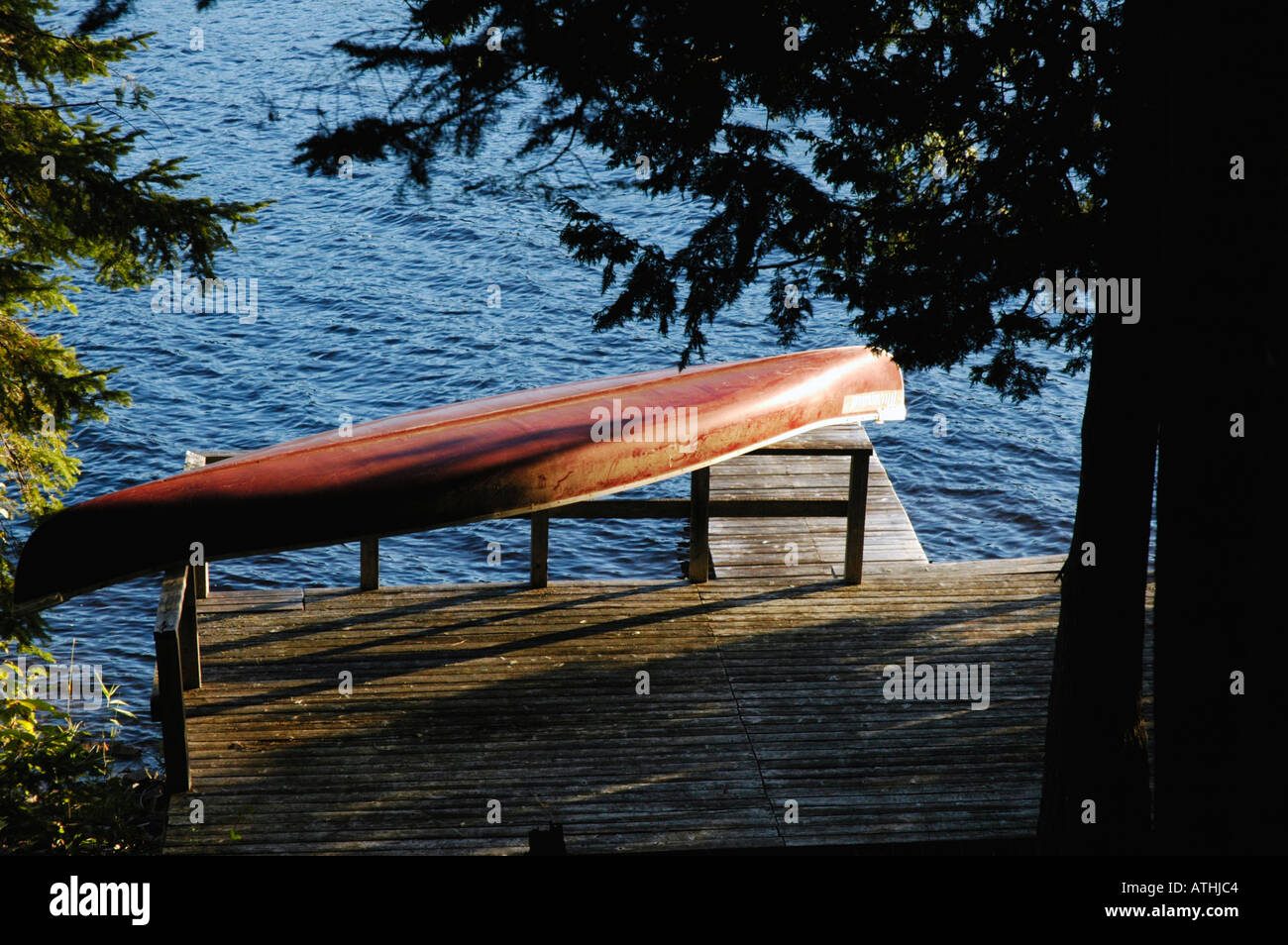 Red canoa sul dock con poco vento e acqua circondata da una foresta Foto Stock