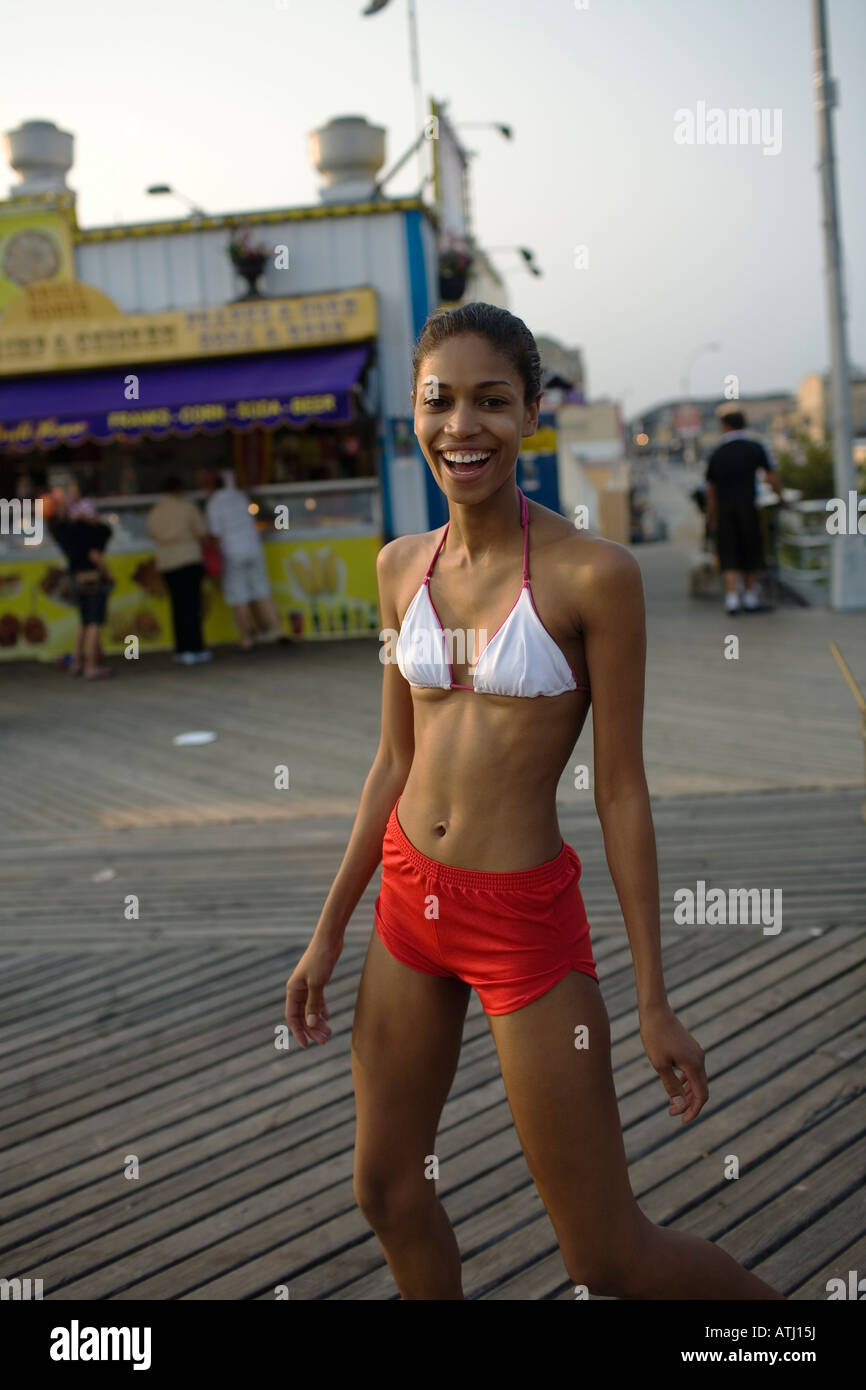 Giovane donna sorrisi come lei cammina sul lungomare a Coney Island Brooklyn Foto Stock