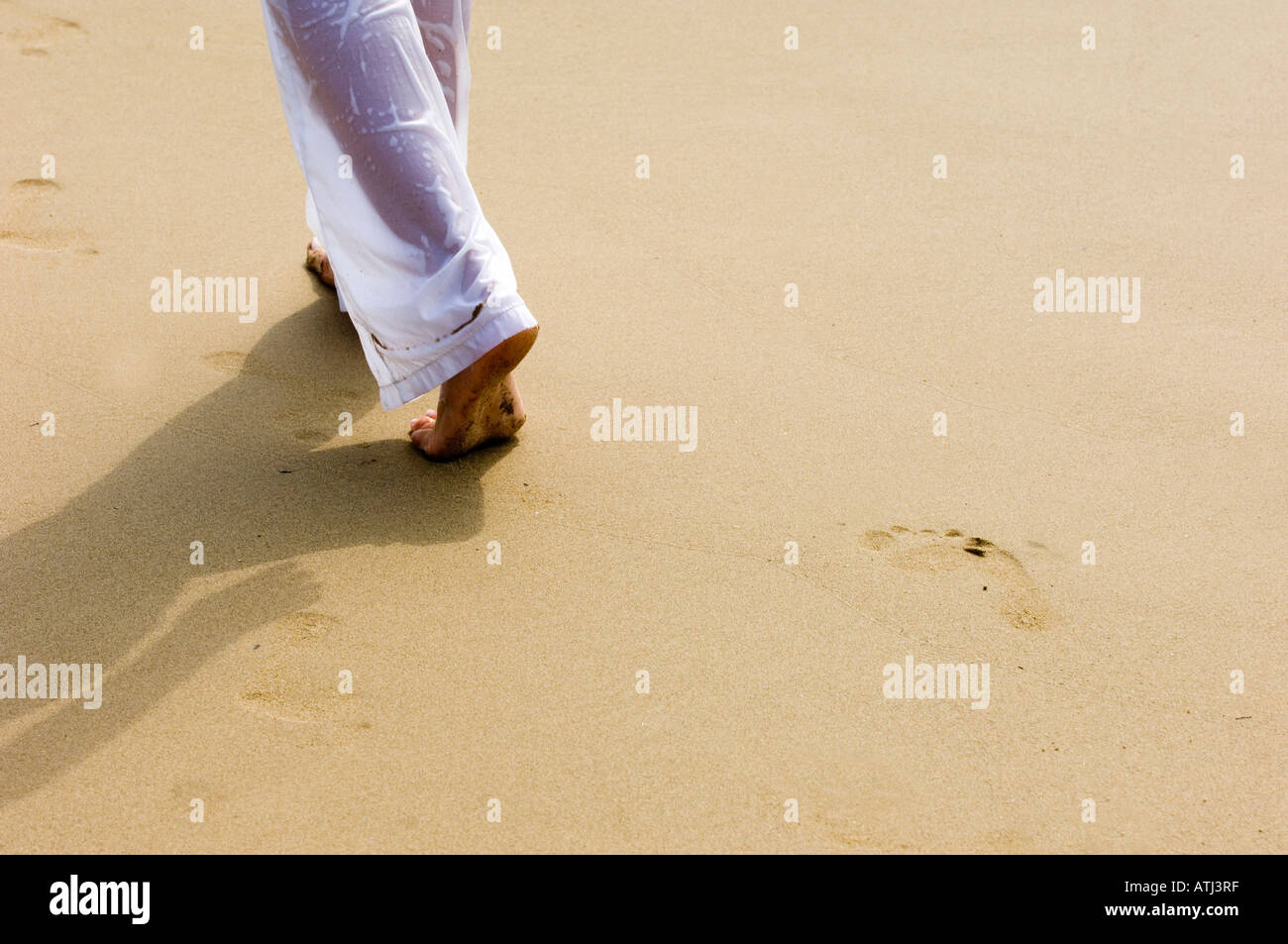 La parte inferiore di una donna che indossa bagnato pantaloni bianchi a camminare sulla sabbia Foto Stock