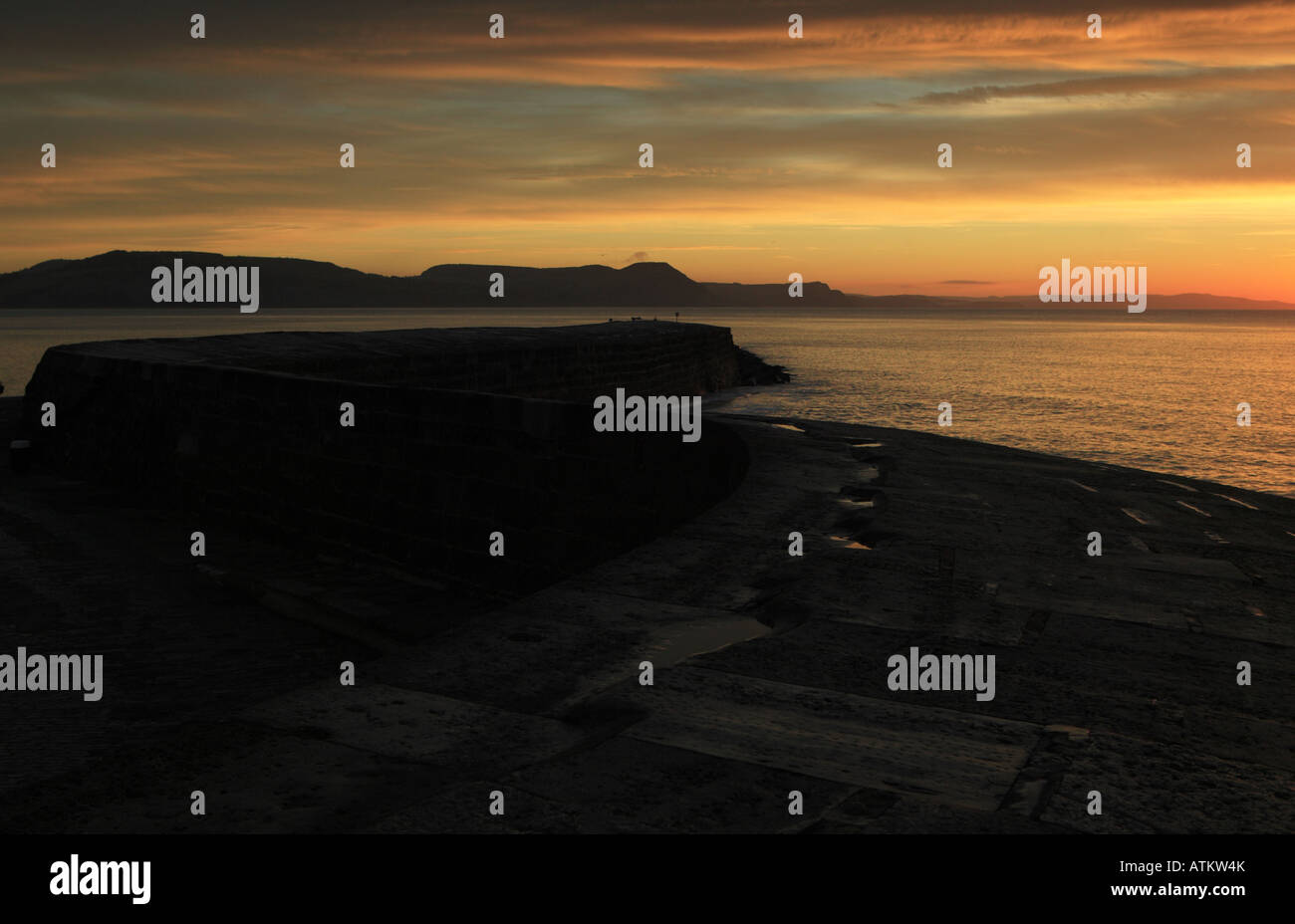 Il cobb a Lyme Regis all'alba in ottobre con vivacemente colorato nubi sul mare scuro, il Cobb crea una curva astratta Foto Stock