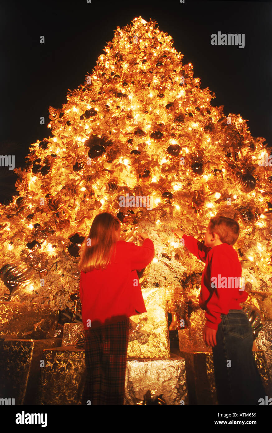 Un ragazzo e una ragazza sotto decorate luminosamente gigantesco albero di Natale Foto Stock