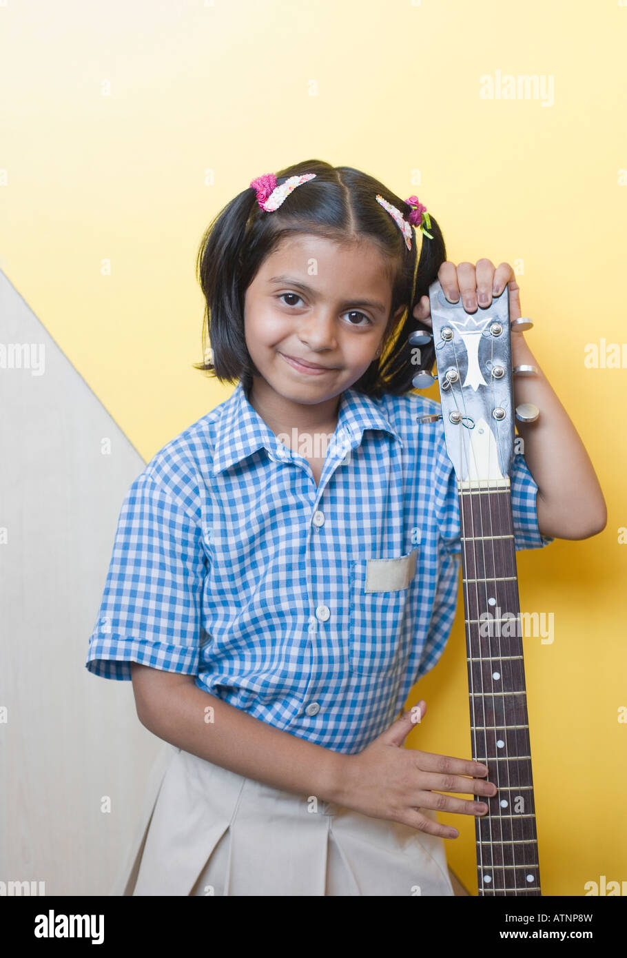 Ritratto di una scolaretta in piedi con una chitarra e sorridente Foto Stock