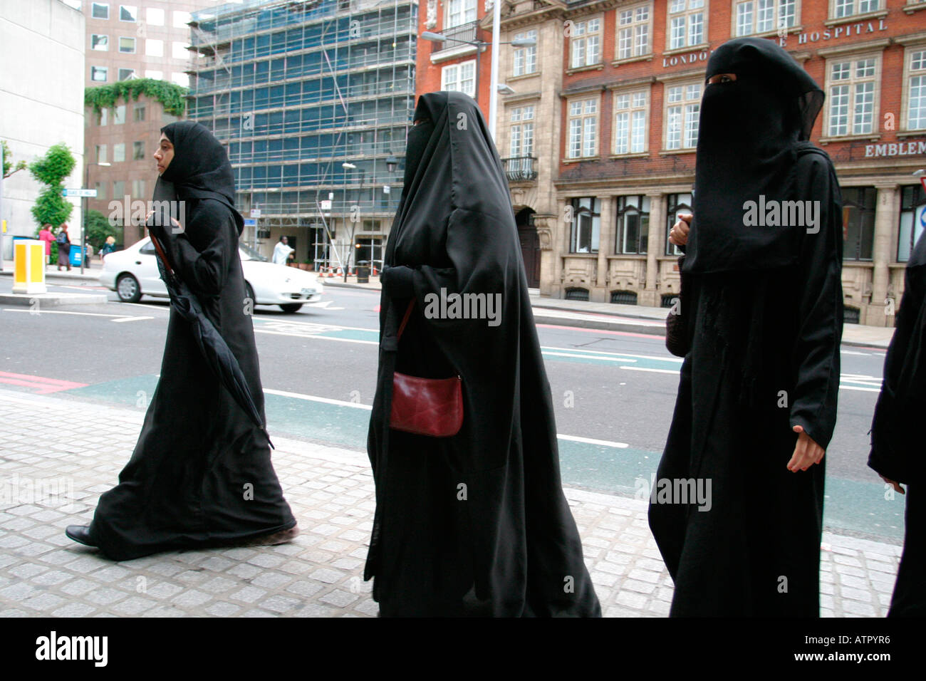 Tre donne a camminare su una strada di Londra su un viaggio di shopping vestita di nero in burka uno portante una borsetta Foto Stock