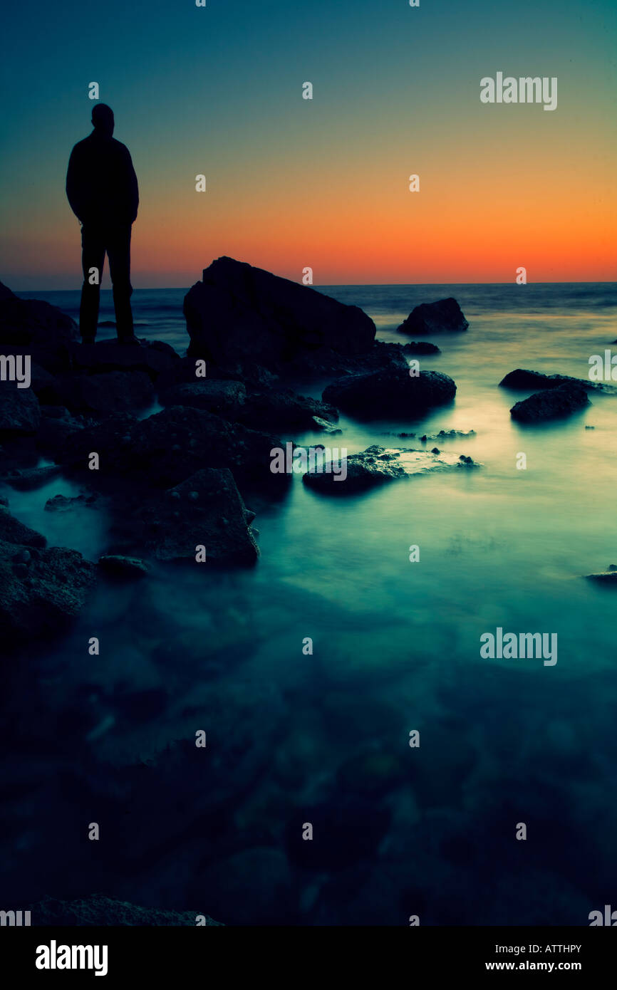 Uomo in piedi sulle rocce che guarda al mare al tramonto Foto Stock