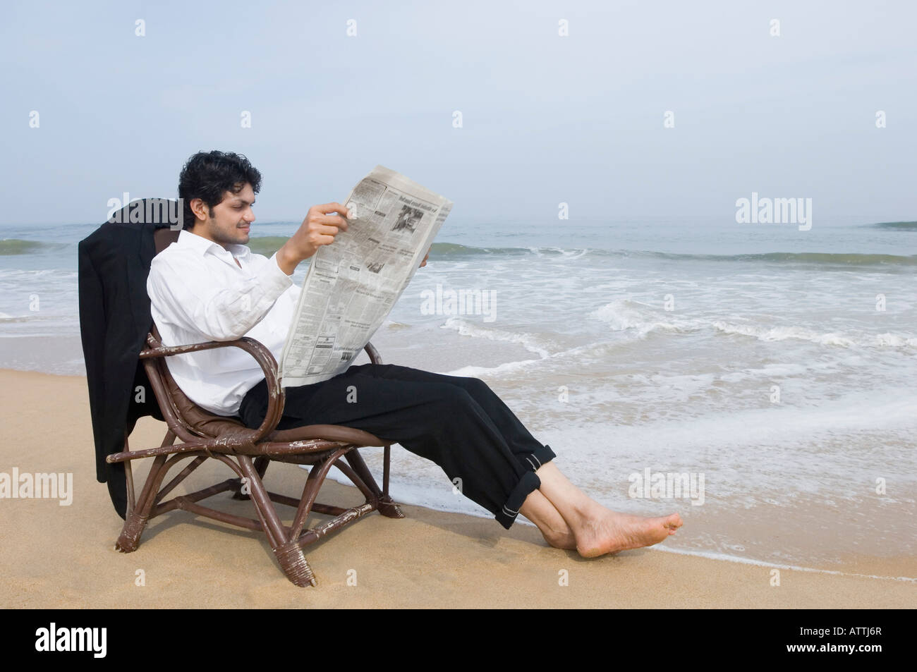 Imprenditore seduto in poltrona e la lettura di un quotidiano sulla spiaggia Foto Stock