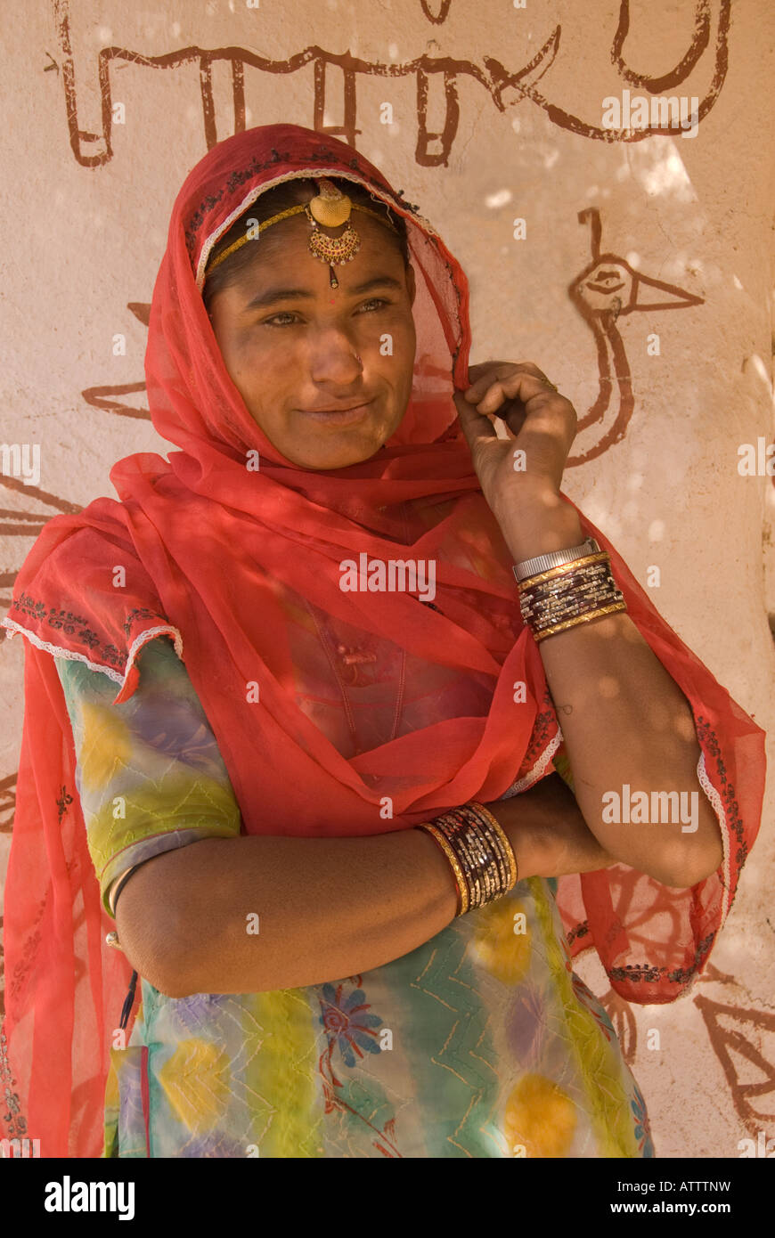 Bella giovane donna indiana adornata con gioielli e indossando un Sari davanti a una parete decorata con pittura primitiva Foto Stock