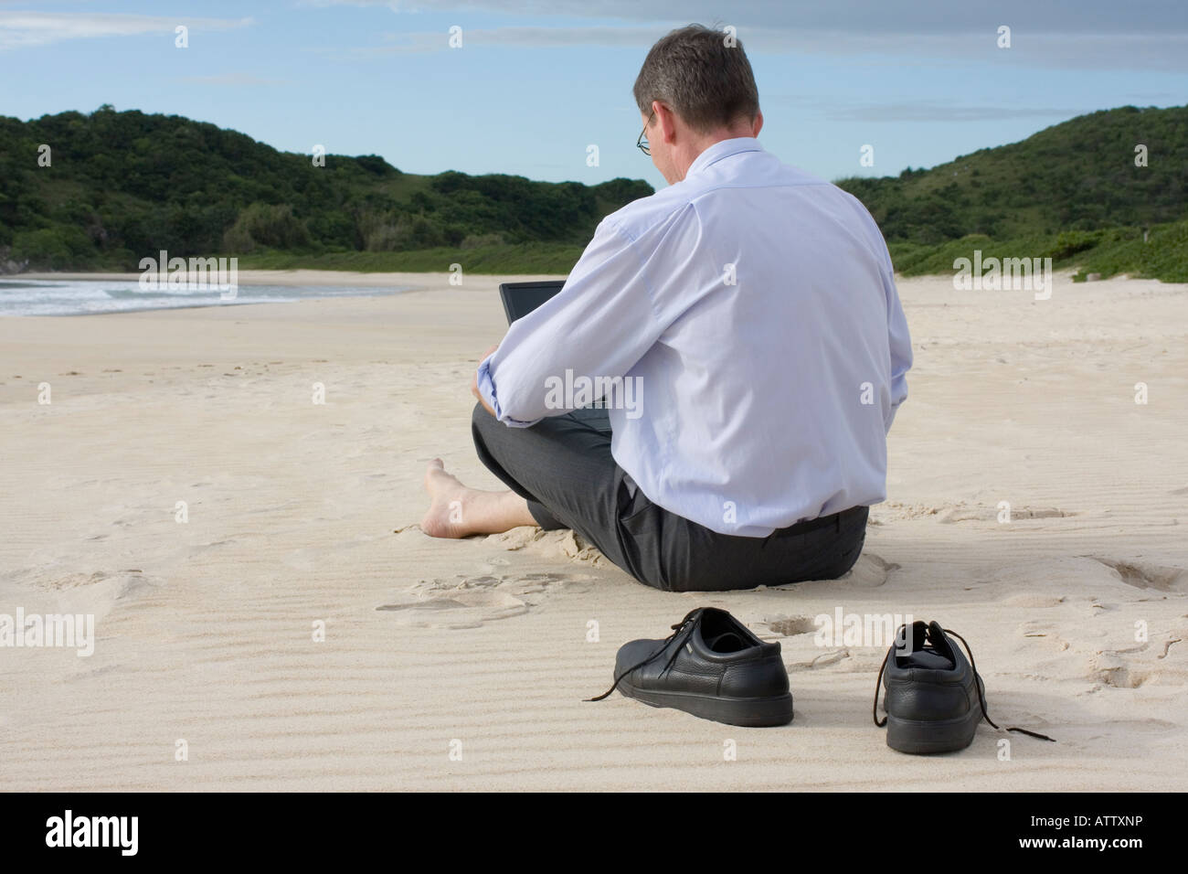 Imprenditore lavora con il suo portatile mentre è seduto a piedi nudi sulla spiaggia Foto Stock