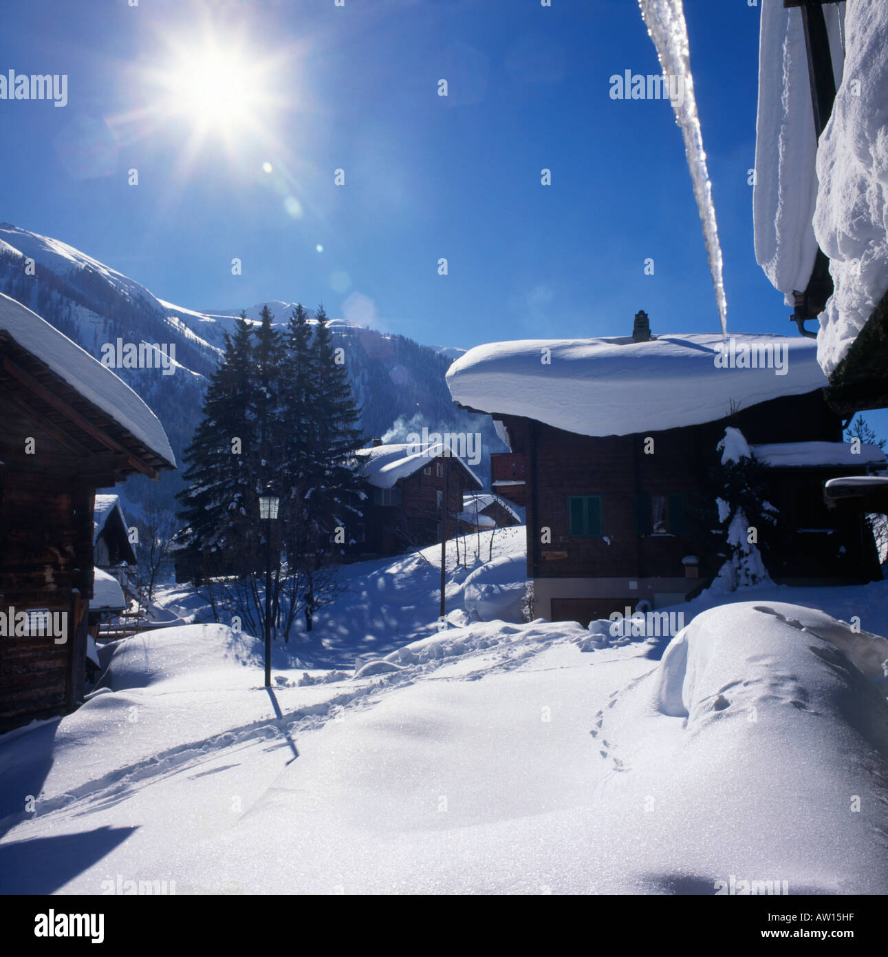 Scatola di cioccolatini vista invernale con neve spessa su tetti chalet & grande ghiacciolo appeso nel villaggio di Bienne Goms svizzera Foto Stock