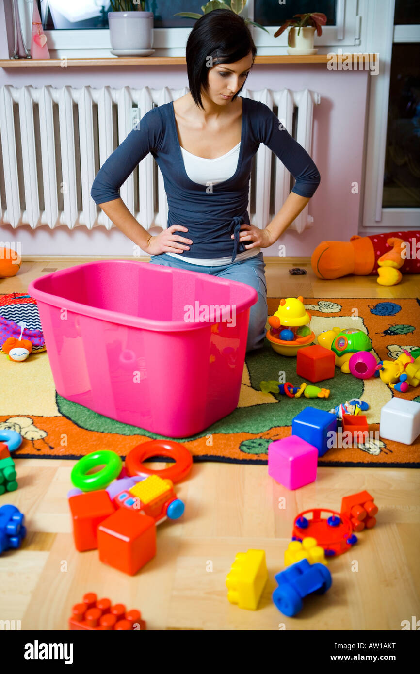 Giovane donna inginocchiata ai container con giocattoli e assembla disseminata giocattoli assomiglia pensato a qualcosa di Vista frontale Foto Stock