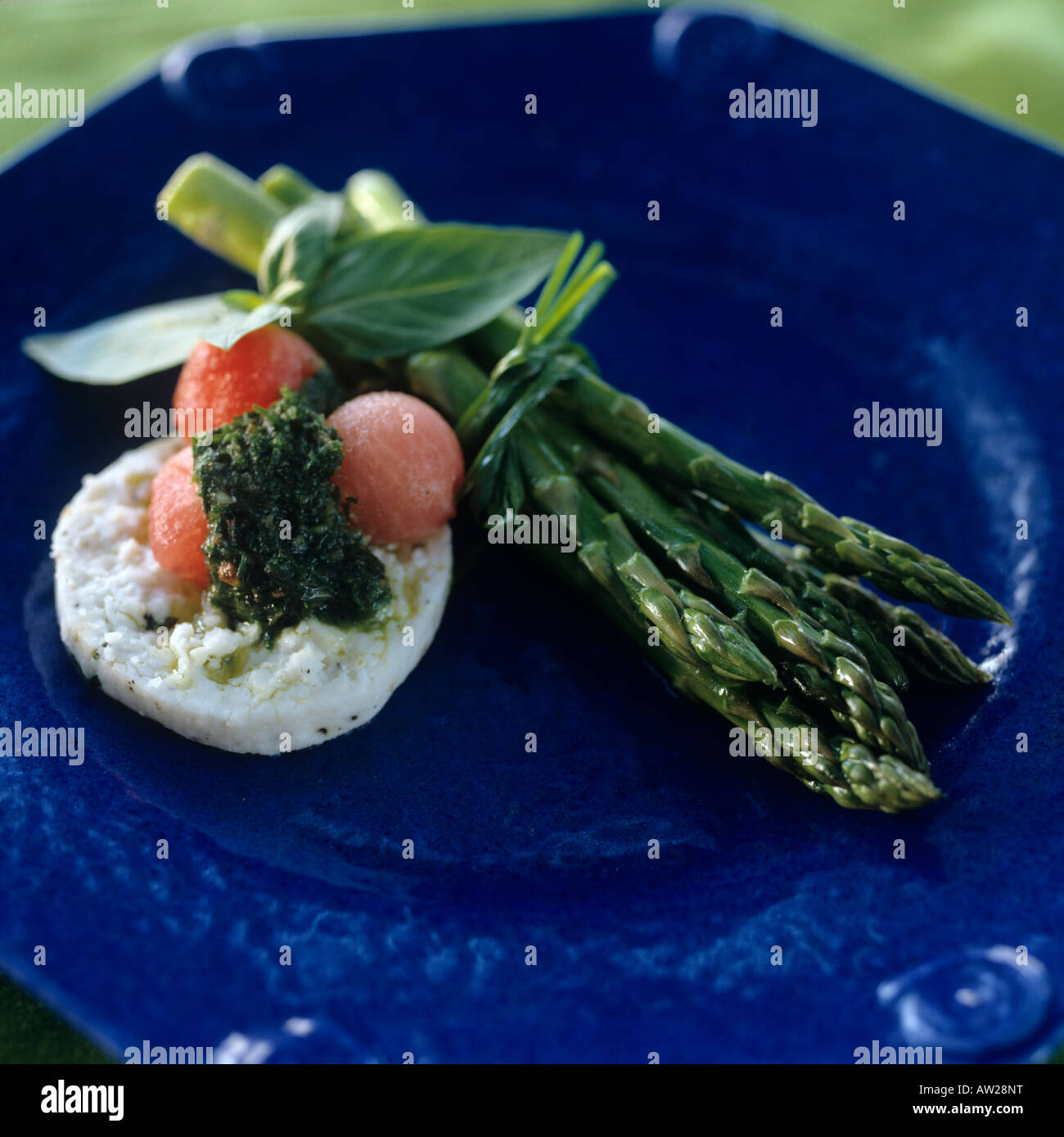 Asparagi con palline di melone, formaggio di capra e basilico su una piastra di colore blu Foto Stock