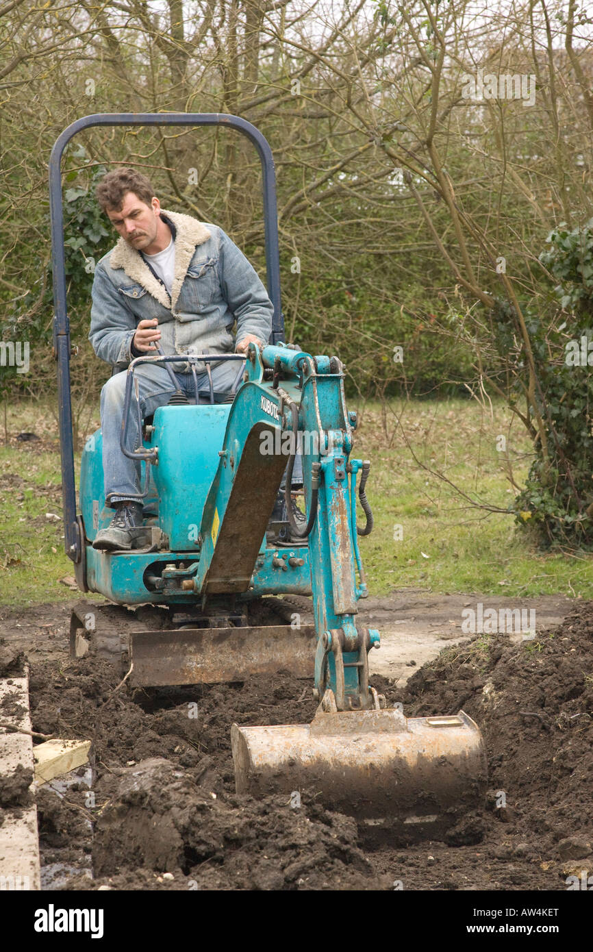 Un uomo alla guida di un mini escavatore / escavatore Foto Stock