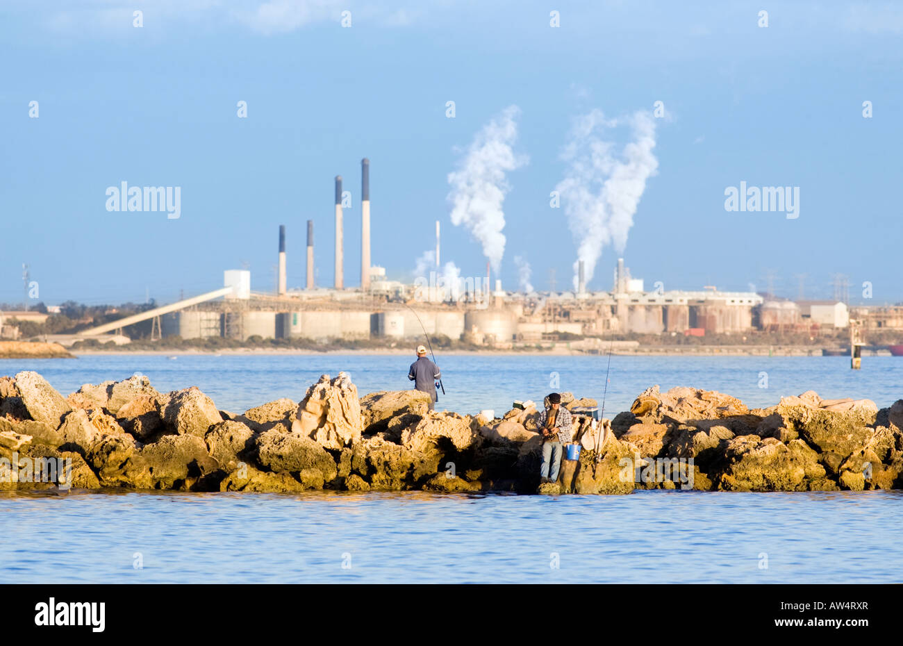 Due uomini la pesca al largo un groyne a Woodman punto con uno sfondo di industria pesante a Kwinana a Perth, Western Australia Foto Stock