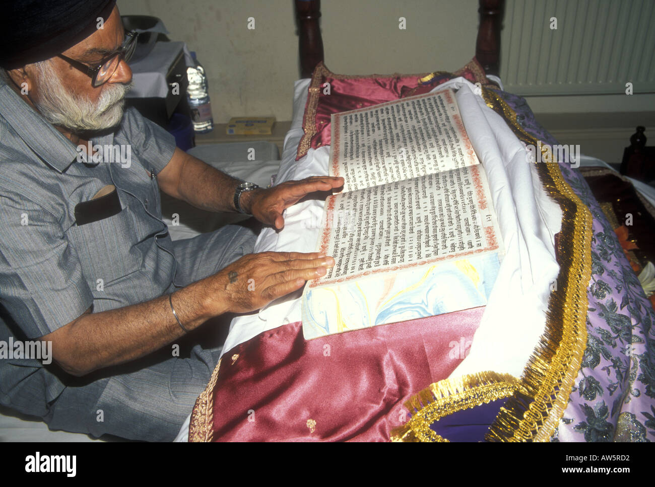 Sikh anziano, o granthi, che legge dal sacro Guru Granth Sahib Foto Stock