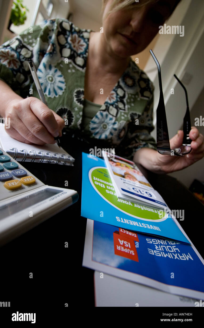 Donna che studia e prende appunti sui volantini dei conti di risparmio individuali ISA sul tavolo con calcolatrice e blocco note Foto Stock