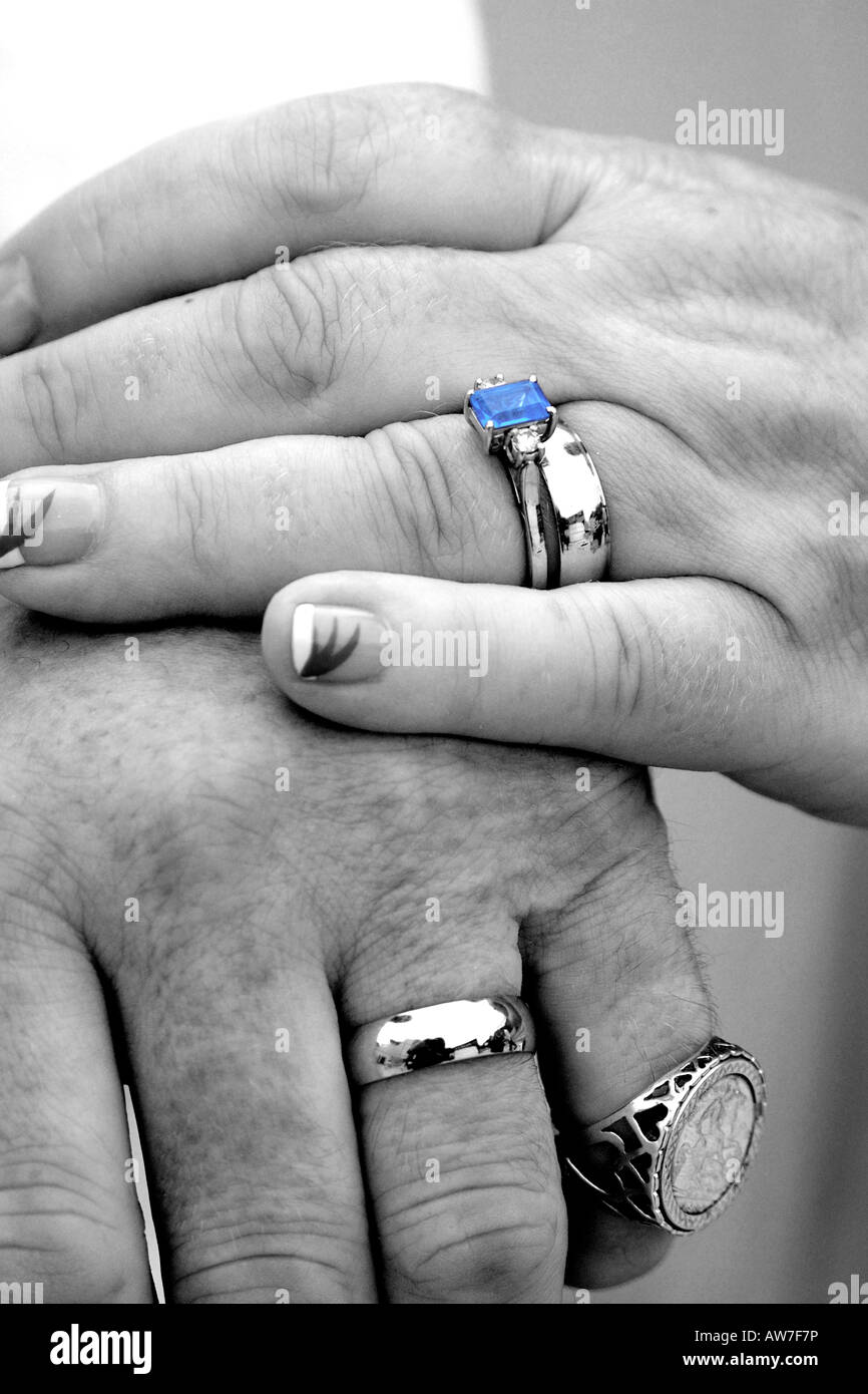 Chiudere fino alle mani di una coppia di novelli sposi mostrando le loro fedi in mono ma con lo zaffiro blu ancora a colori Foto Stock