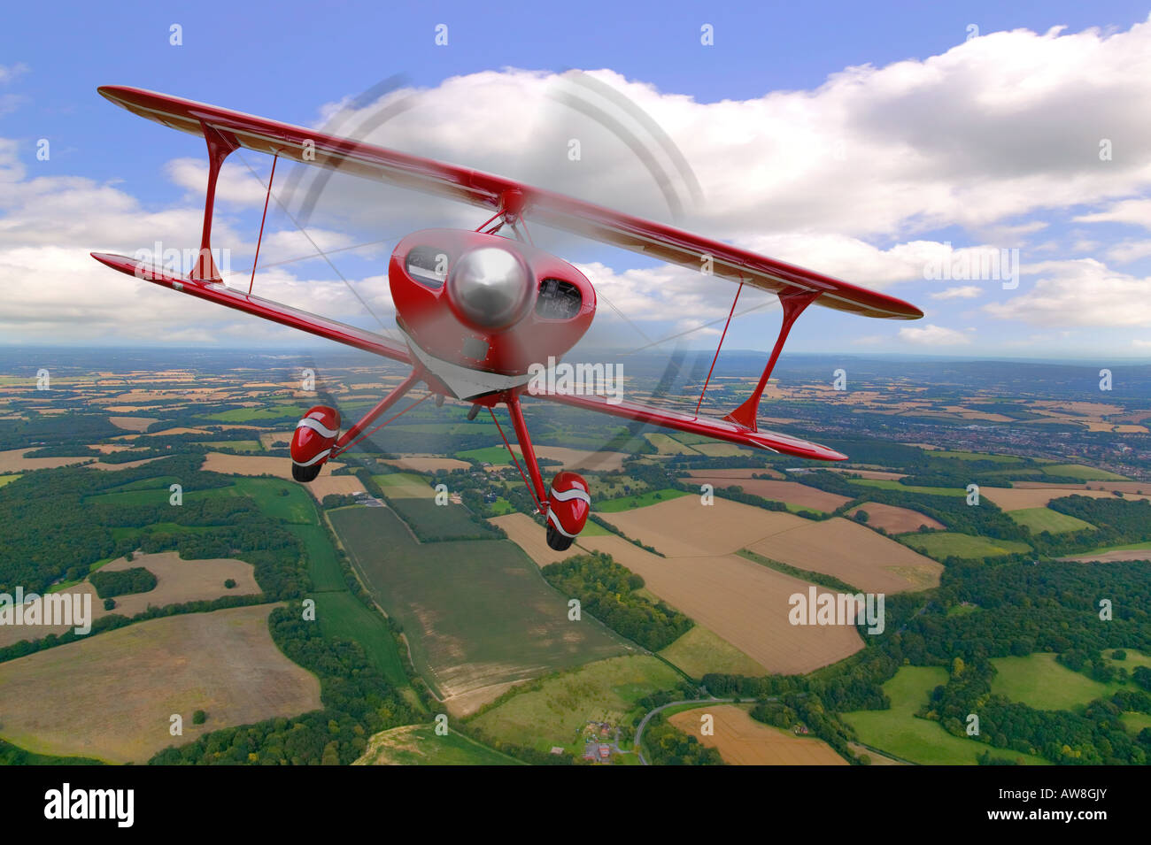 Un rosso biplano acrobatico in volo sopra il paesaggio rurale Foto Stock