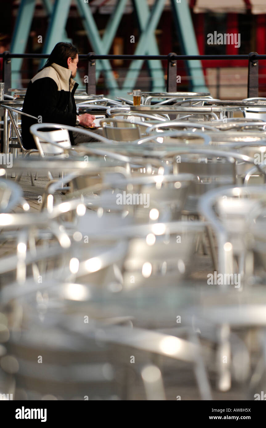 Una donna Uomo seduto da solo al di fuori di un ristorante cafe in strada con fuori fuoco defocussed tavoli e sedie nel foregroun Foto Stock