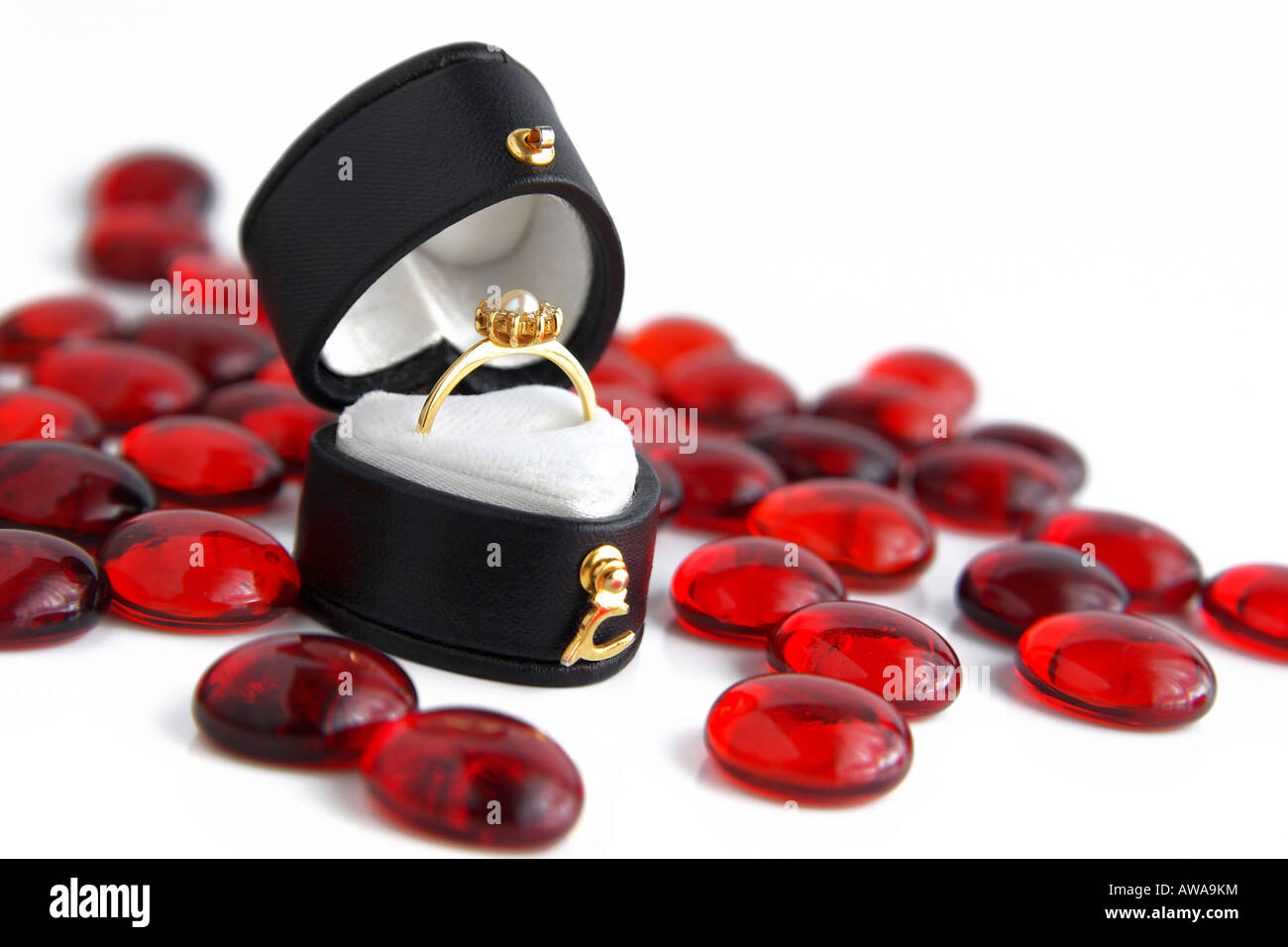 Foto di un cuore a forma di scatola nera con anello di fidanzamento in oro e con una perla sulla parte superiore, circondato da little red pietre di vetro. Foto Stock