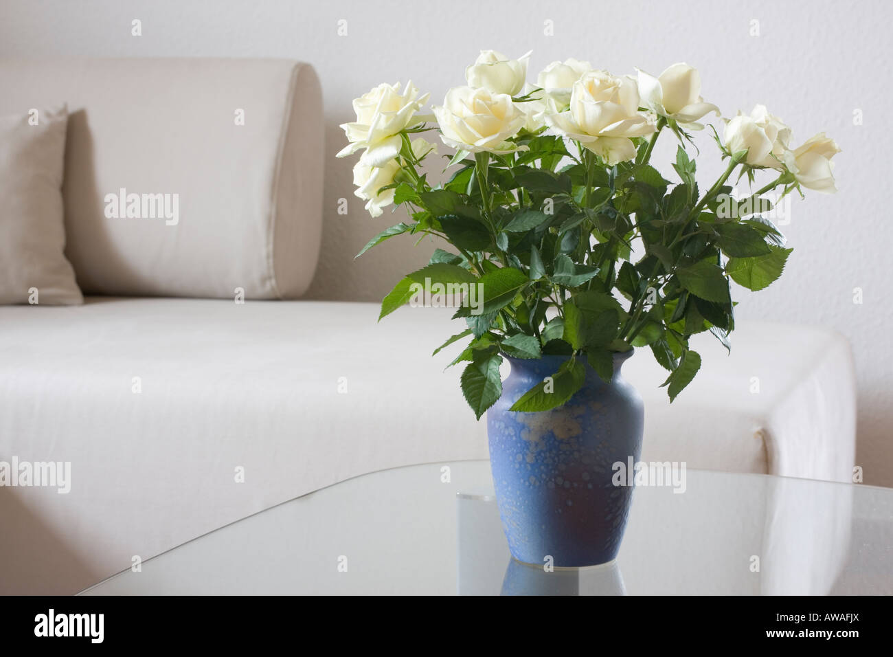 Rose bianche su un tavolo di vetro nel salotto luminoso Foto Stock