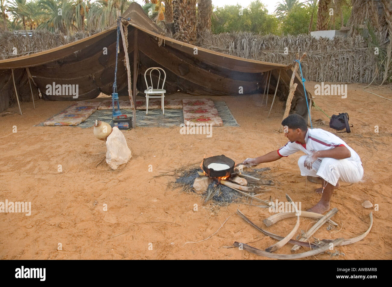 Un uomo la cottura nella parte anteriore di una tenda in oasi di Ksar Ghilane, nel deserto del Sahara del sud della Tunisia. Foto Stock